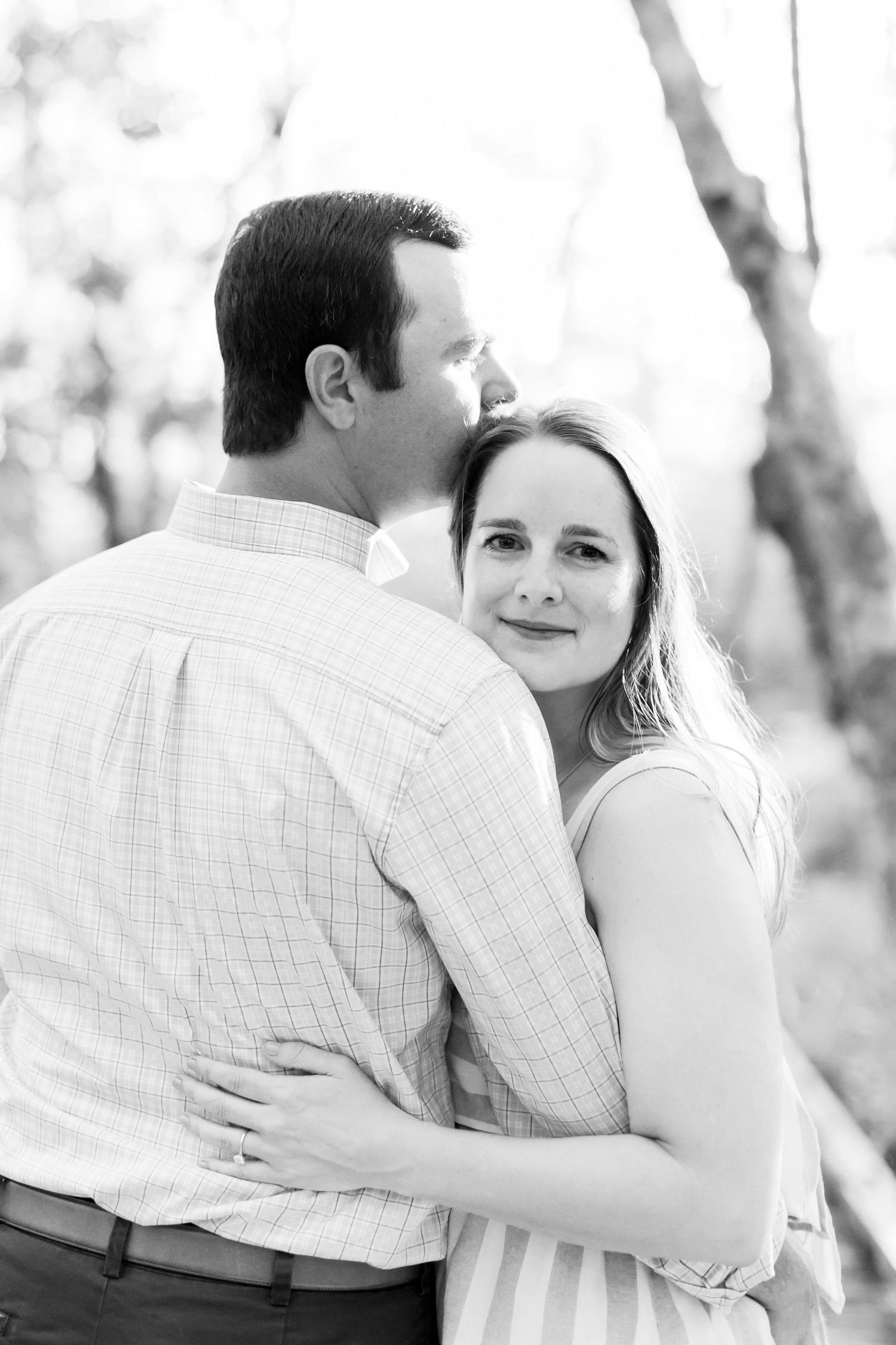Romantic couple embracing on a sunlit forest path during an outdoor photo session.