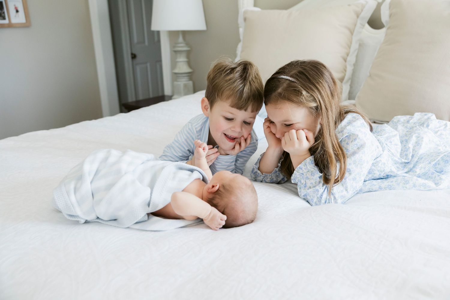 Two children in light blue pajamas share a laugh while lying on a white bed.