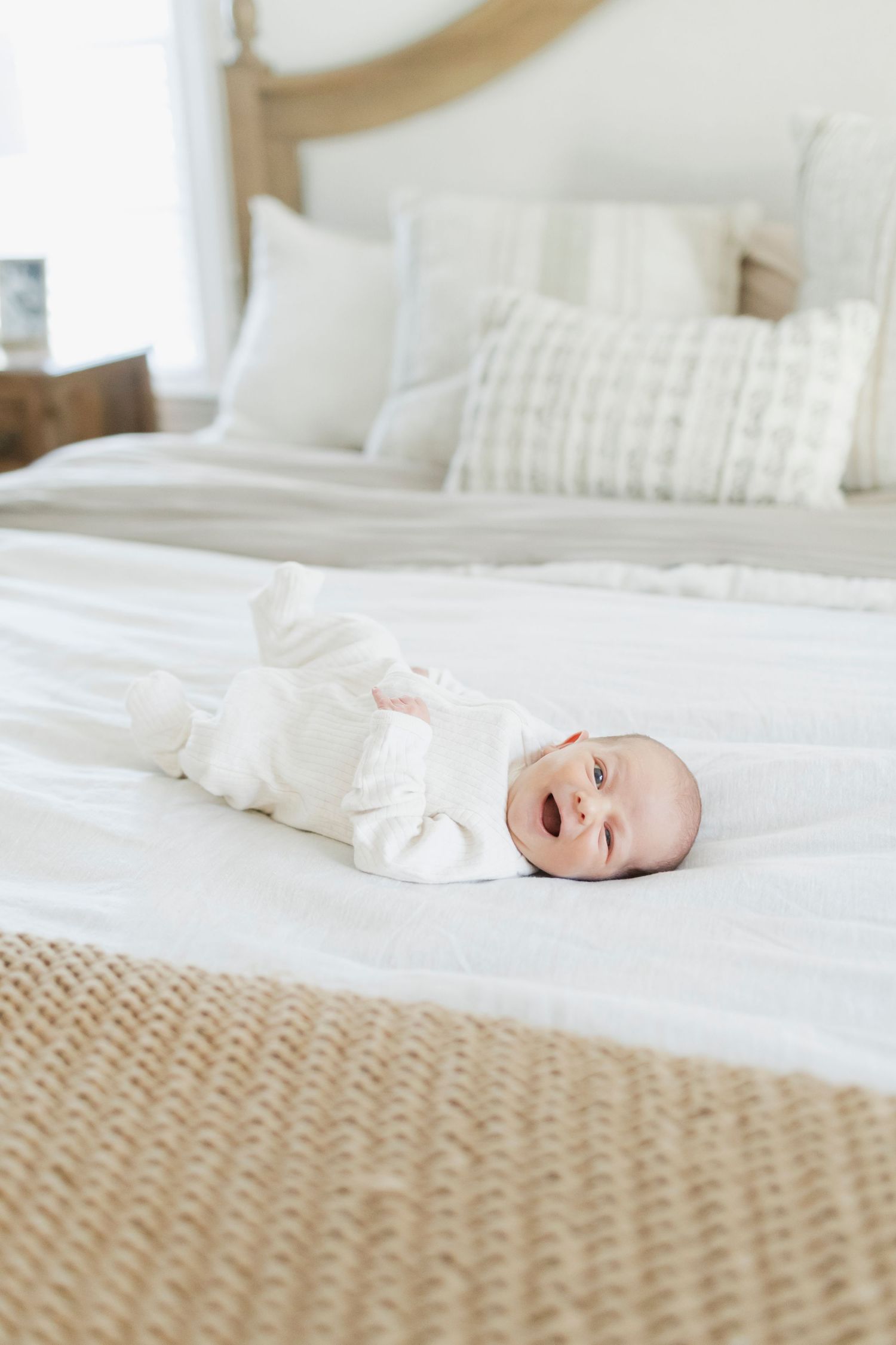 Baby lying on white bedding with textured rug visible.