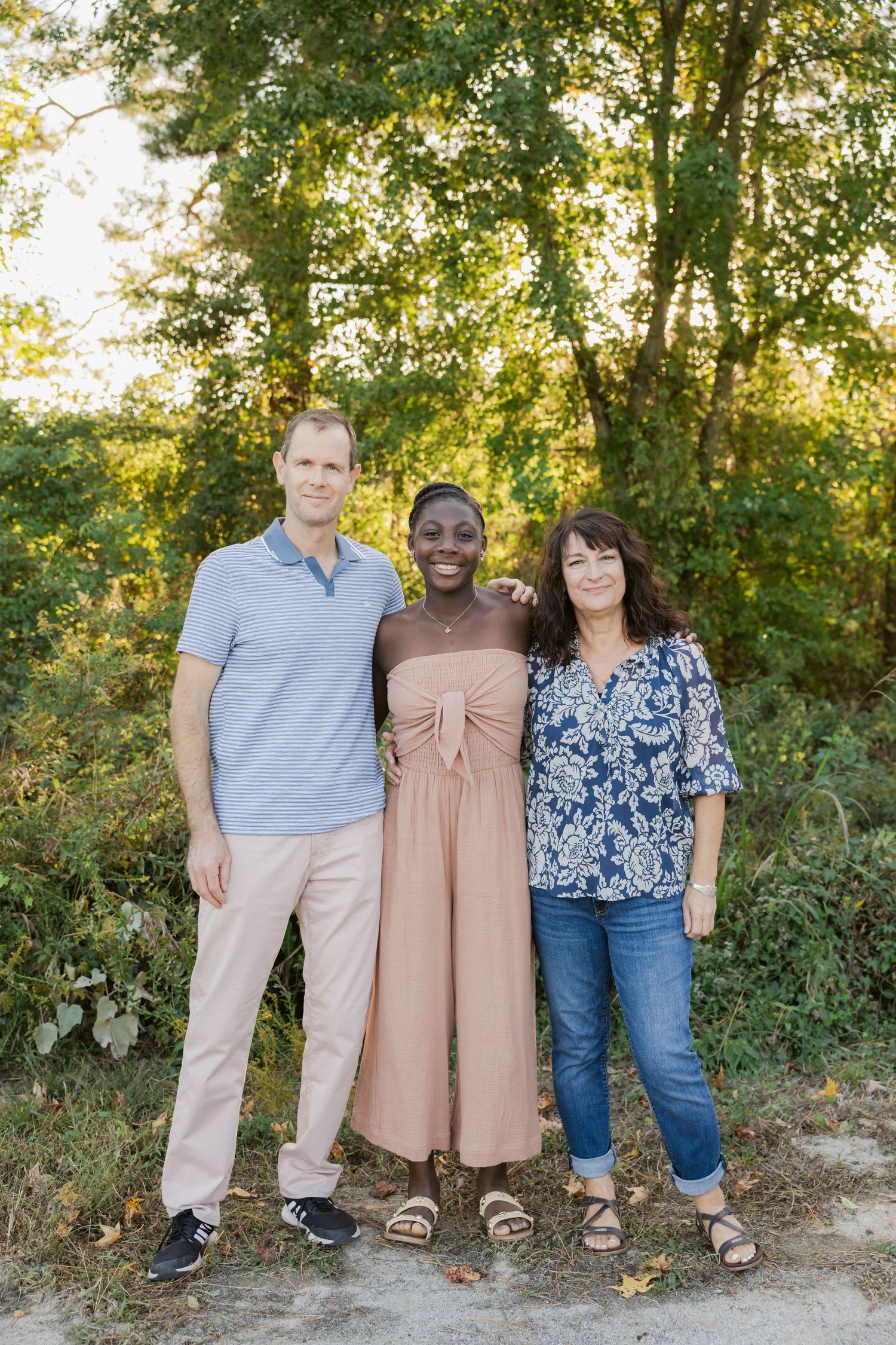 Group portrait of people standing against a leafy green background outdoors.