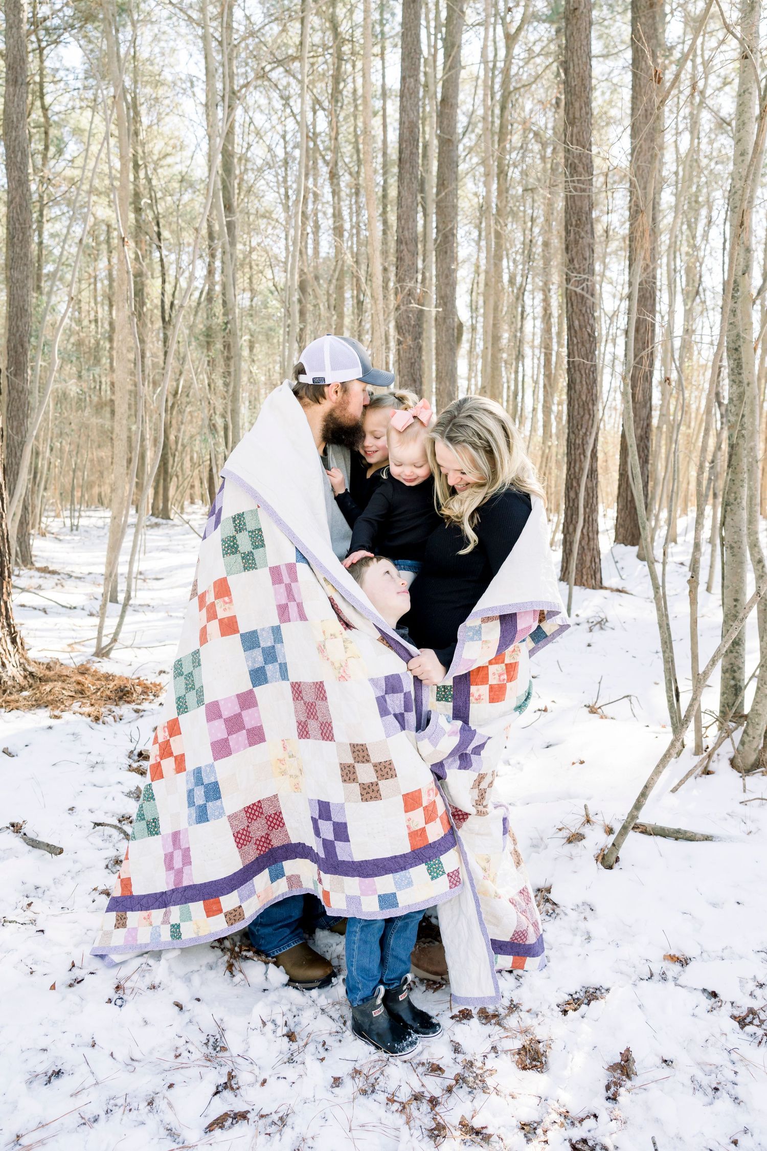 People displaying colorful patchwork quilts in a snowy winter forest setting.
