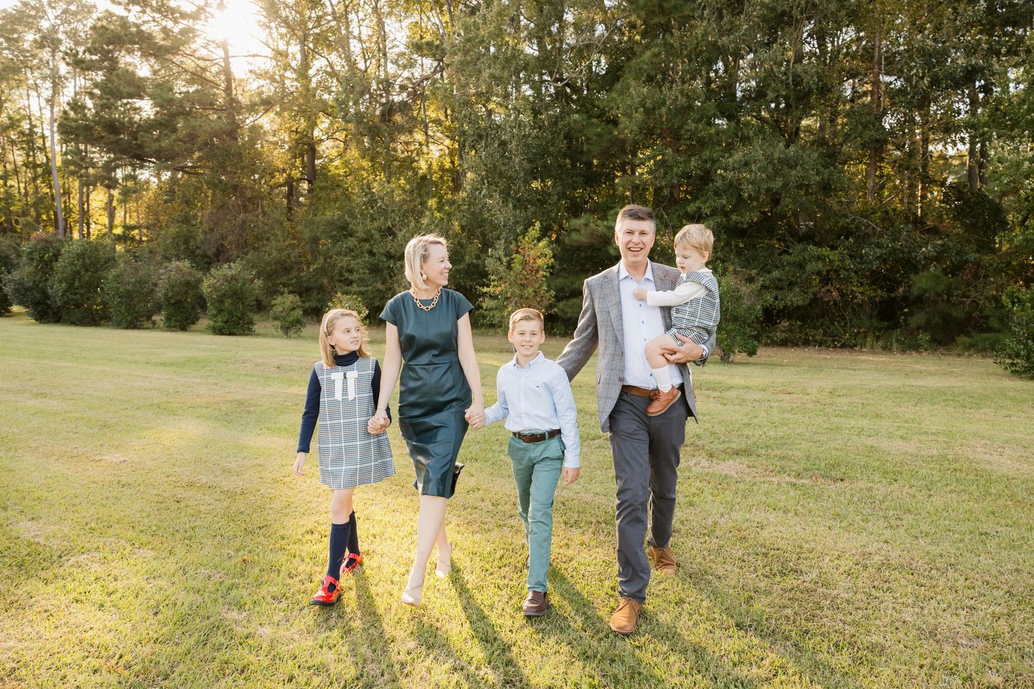 Family walking together in a sunlit grassy field during golden hour.