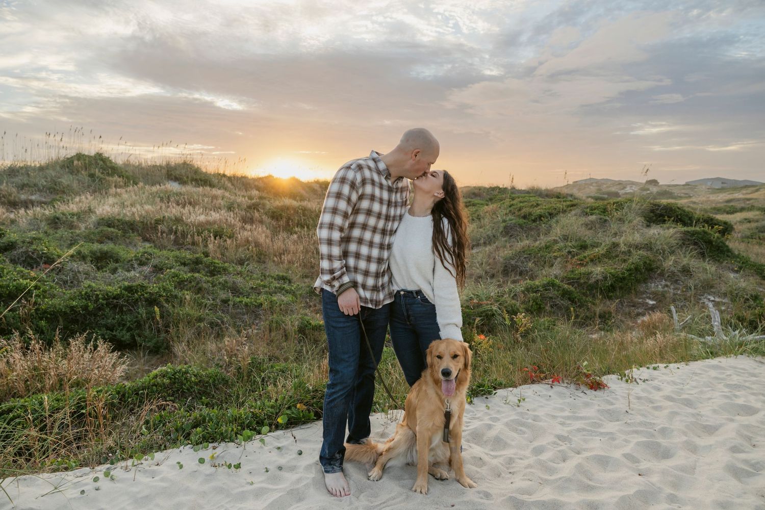 A golden retriever and its owners enjoy a sunset walk along a scenic beach path.