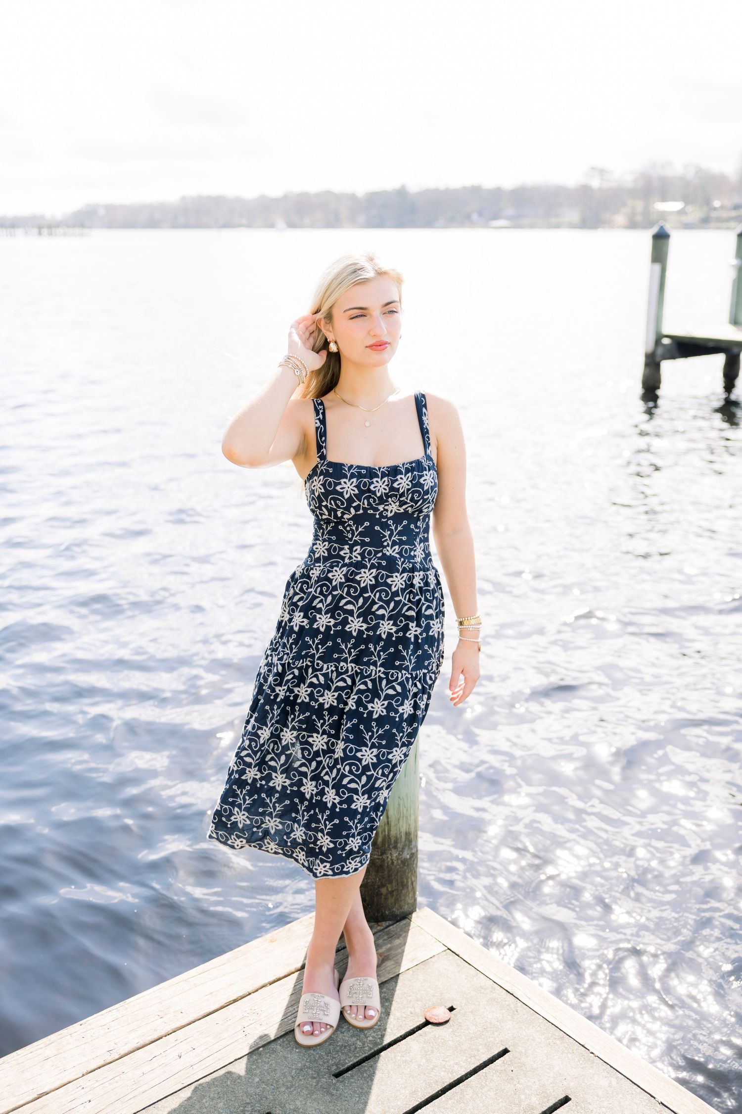 Person in patterned sundress sitting on wooden dock by sparkling water.