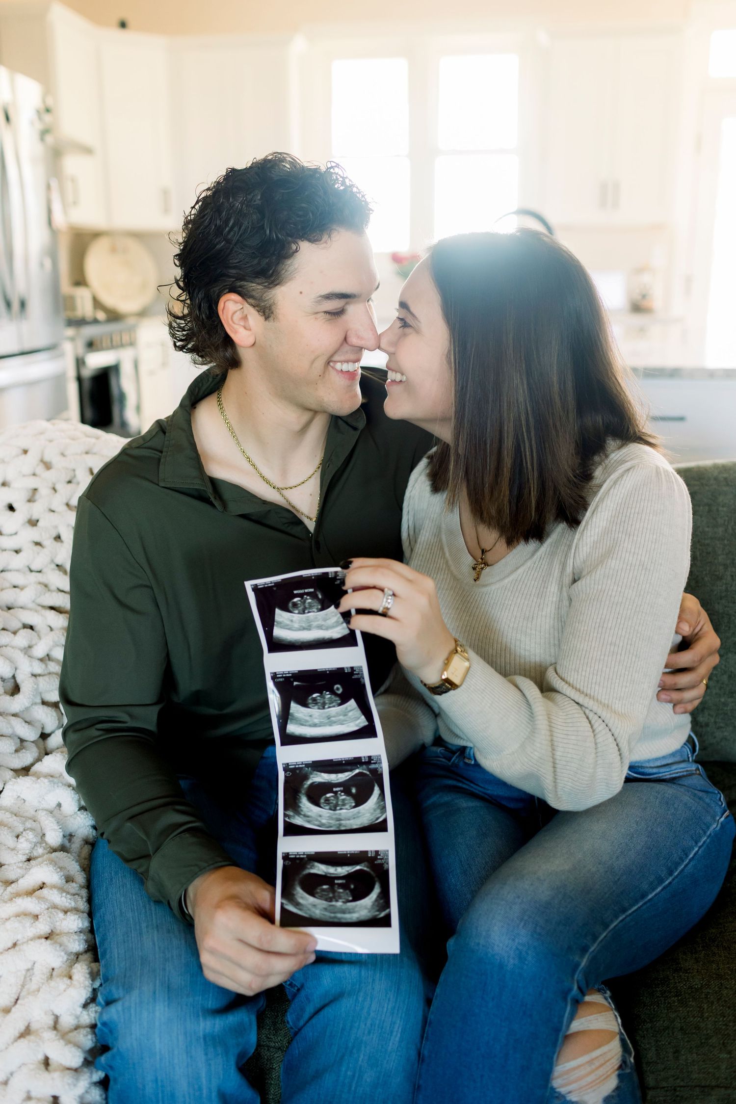 A couple shares intimate moments while holding ultrasound photos in a bright indoor setting.