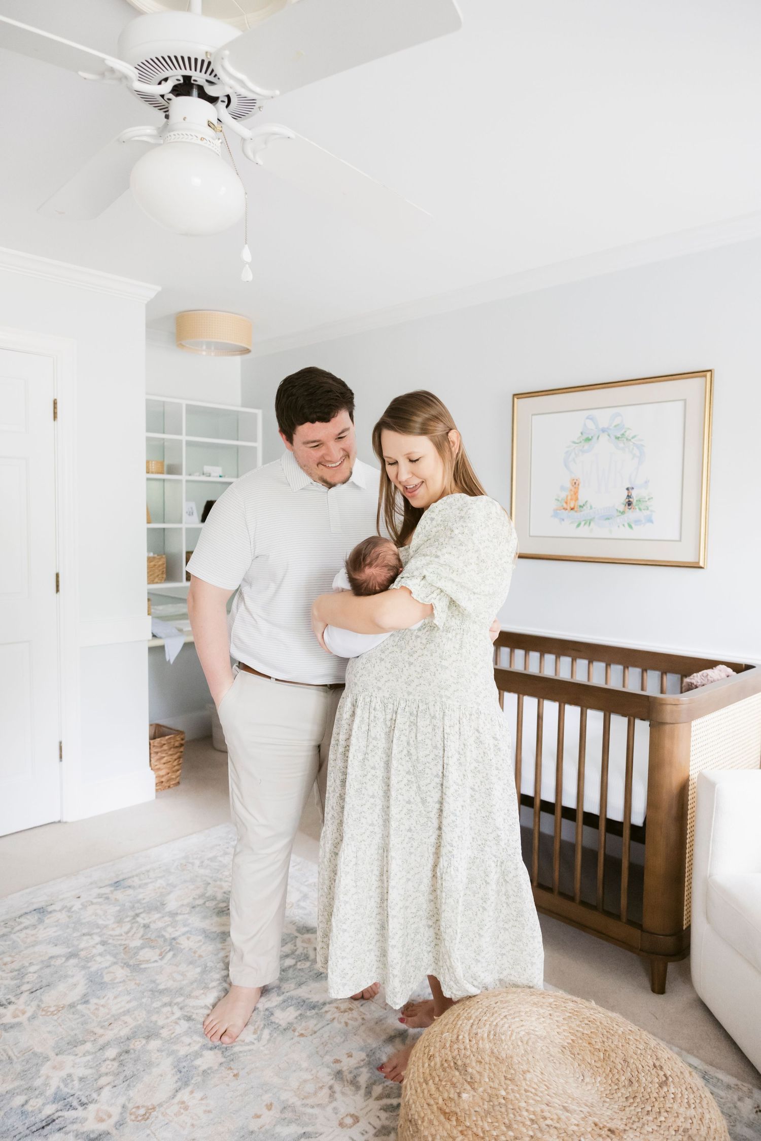 A couple stands in a nursery with their newborn baby near a wooden crib.