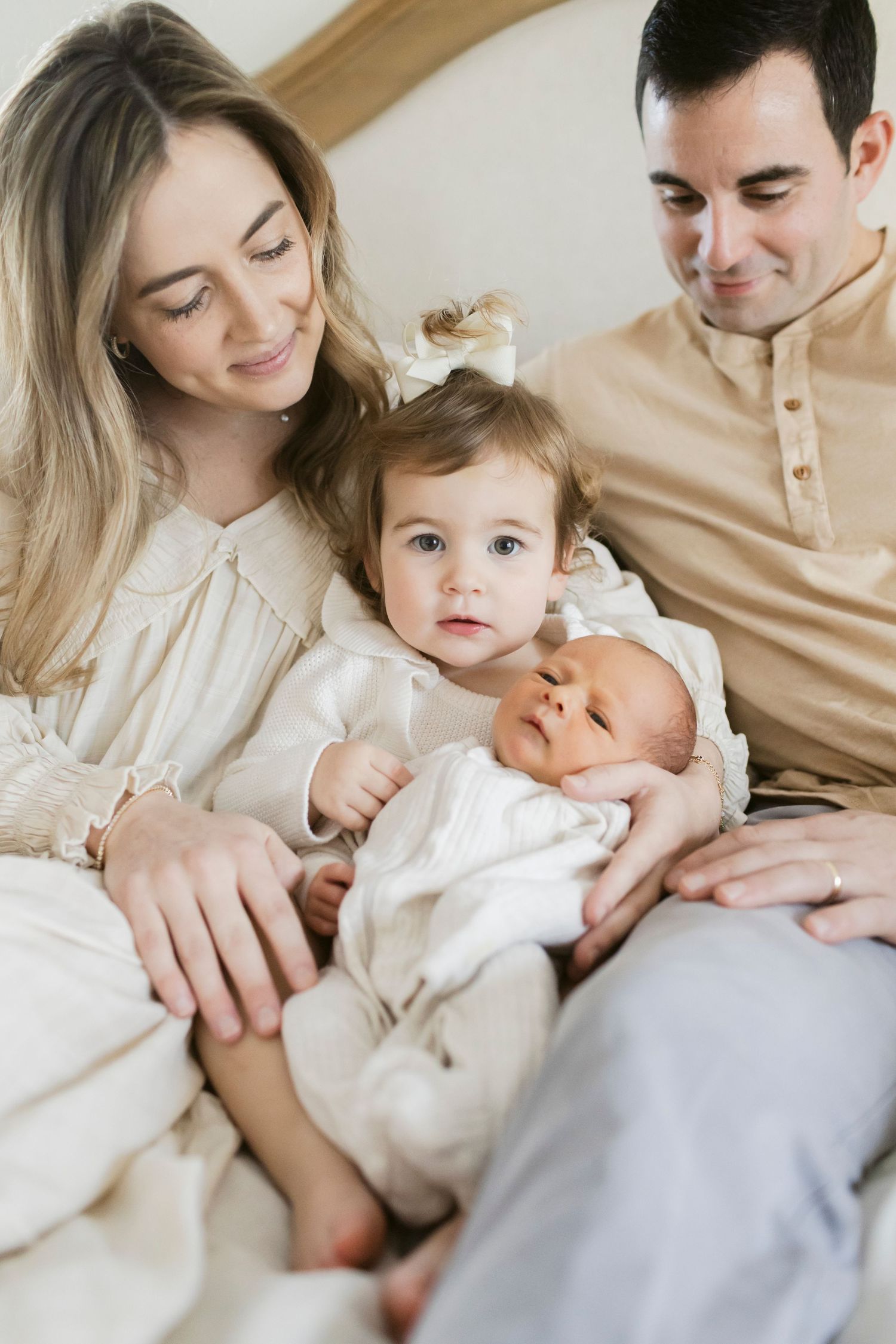 A family of four sits together on a couch, with two young children in white outfits.