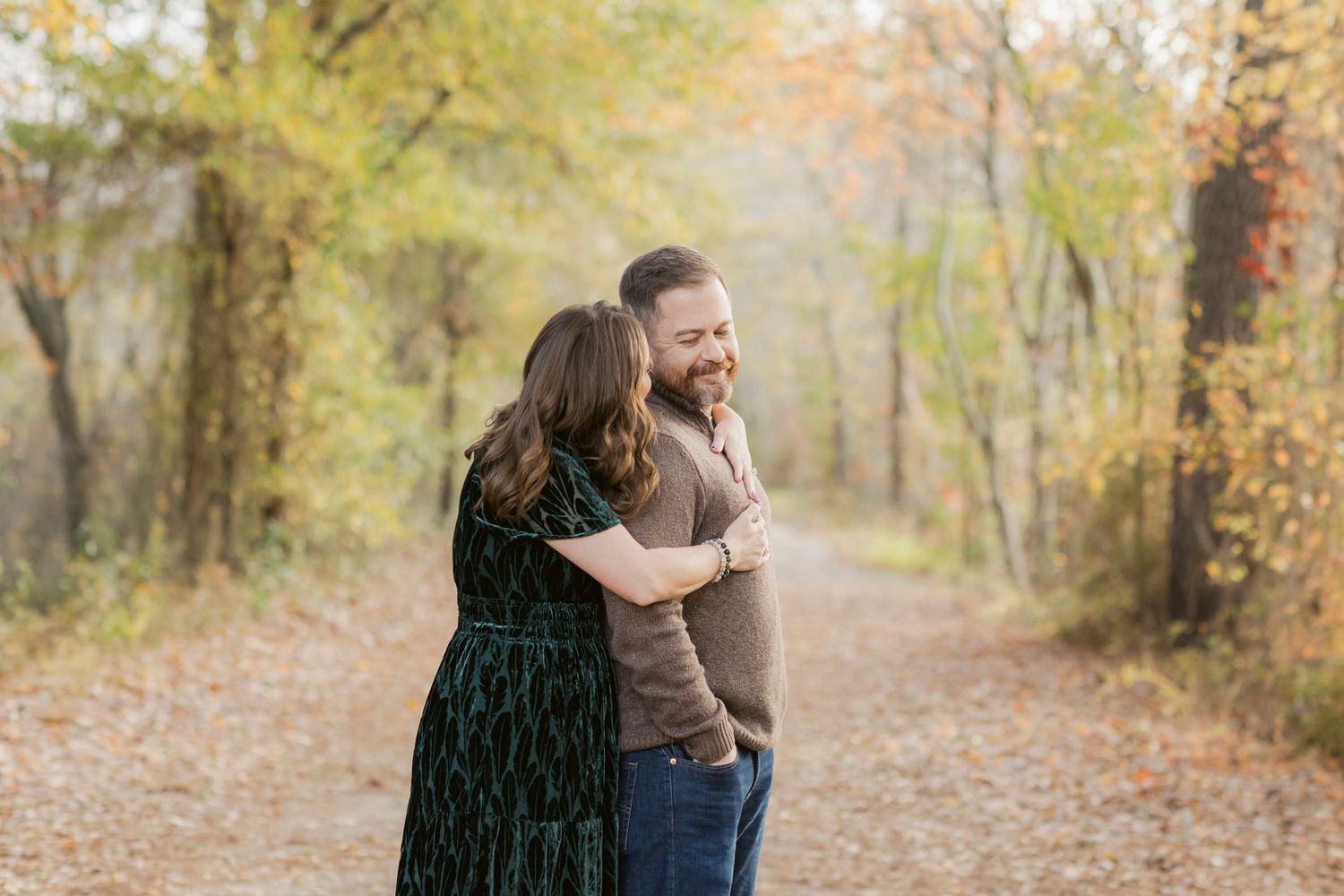 A couple embraces while laughing together on an autumn path surrounded by golden trees.