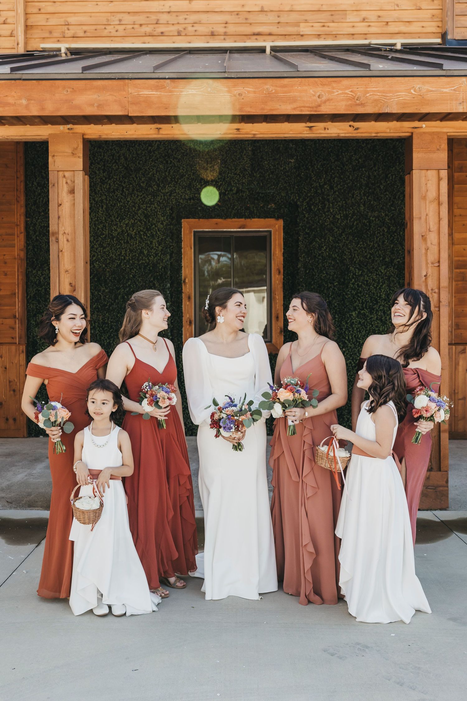 Bridal party in white and terracotta dresses poses together on a covered patio.