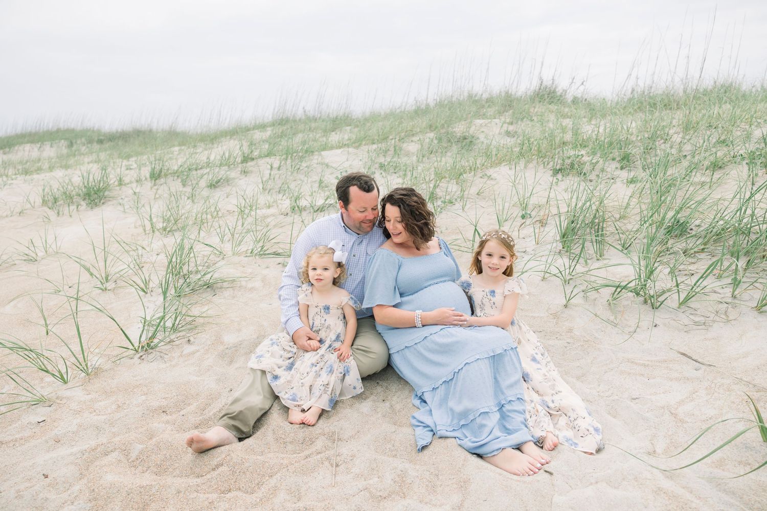 Family relaxing together on sandy beach dunes during golden hour.