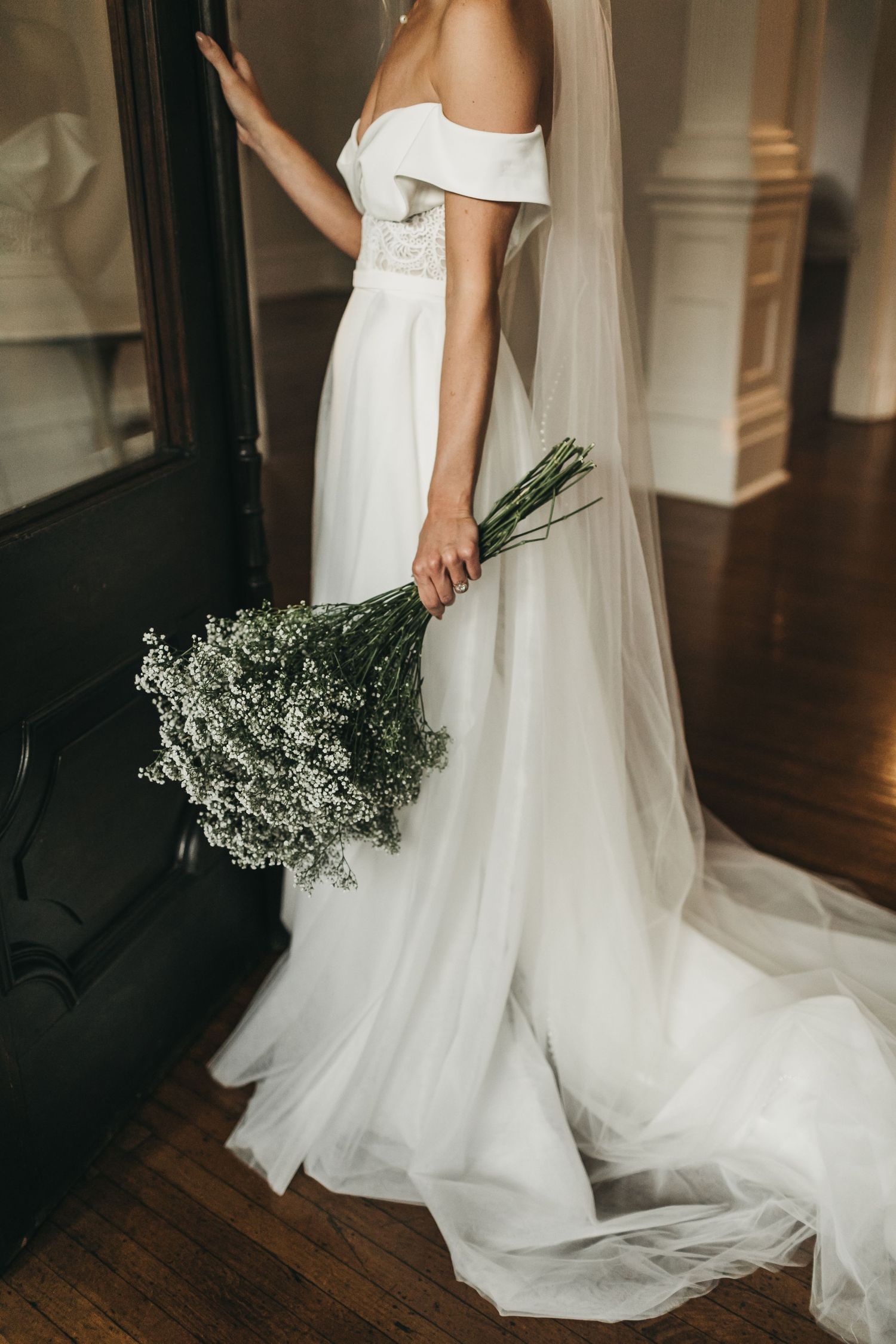 Close-up of a bride holding a delicate baby's breath bouquet with her white dress flowing behind.