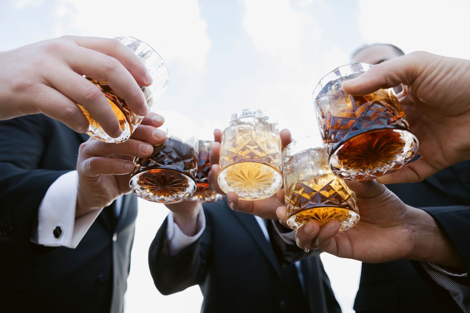 Wedding guests toasting with drinks in an artistic sequence of hands clinking glasses.