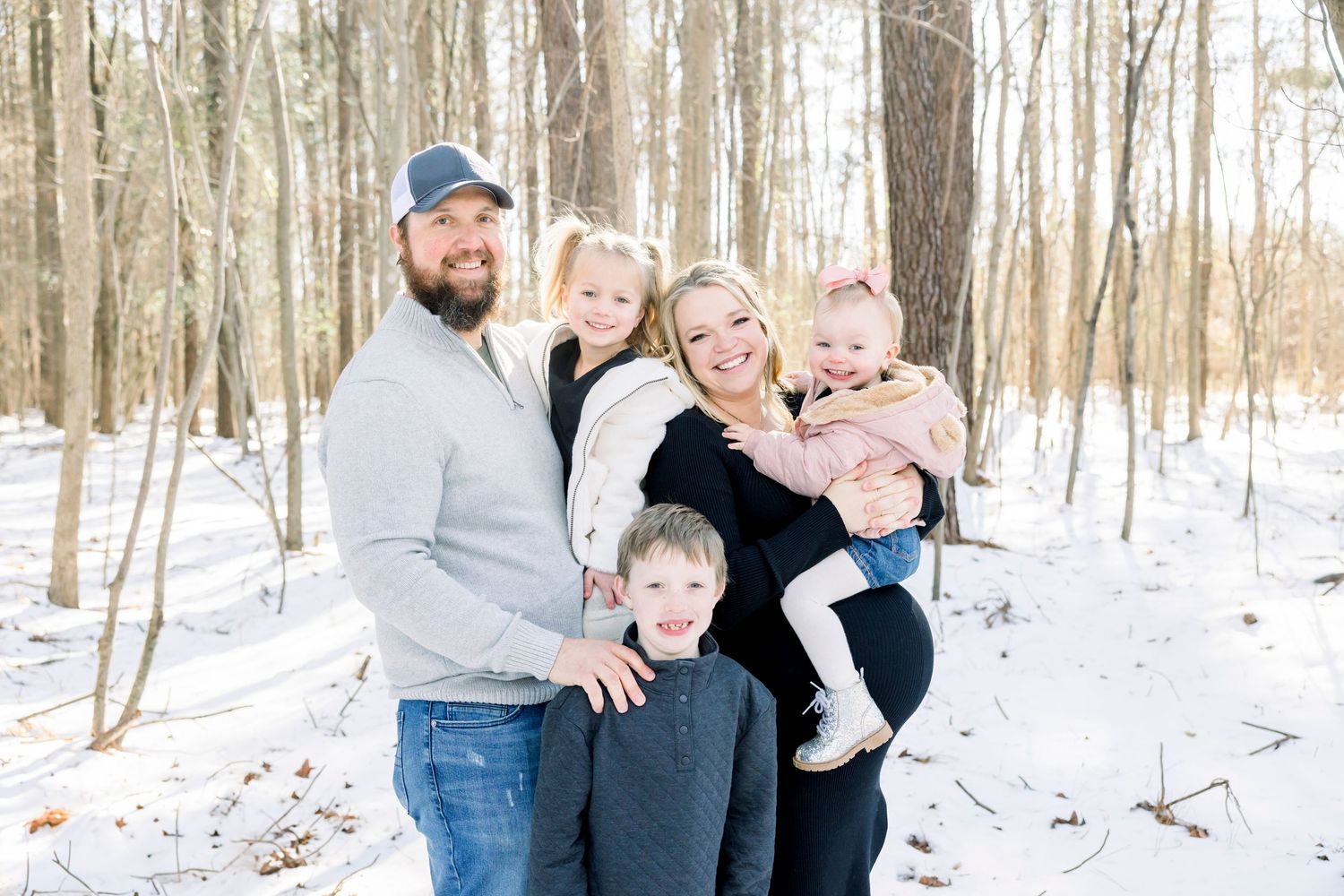 Winter family portrait session in snowy forest with bare trees.