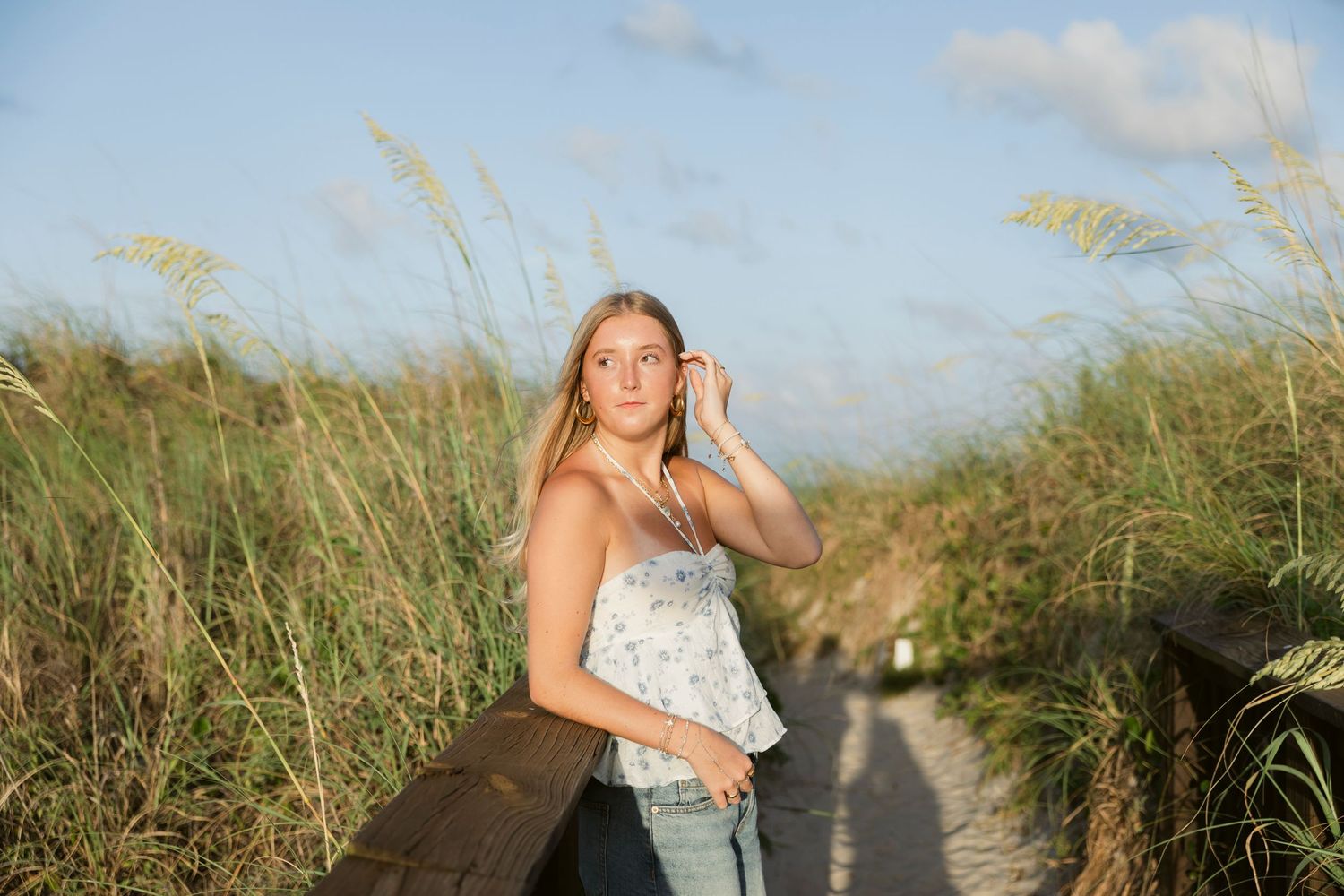 A scenic beach photoshoot at sunset with tall grass and sand dunes in the background.