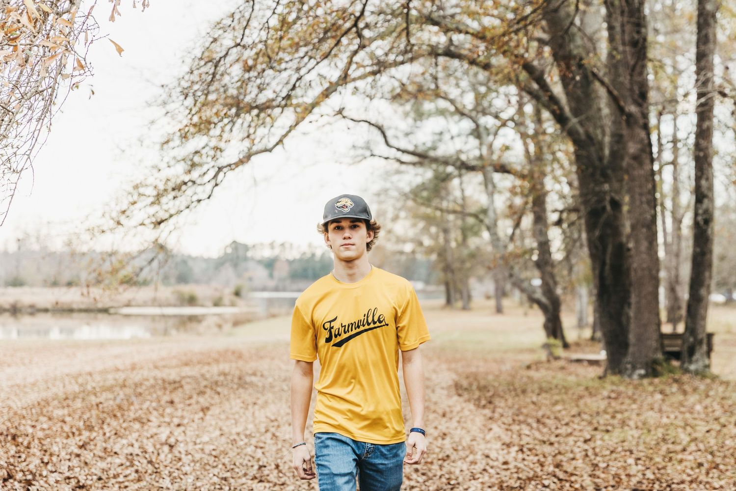 Person wearing yellow t-shirt poses in autumn forest setting with fallen leaves.