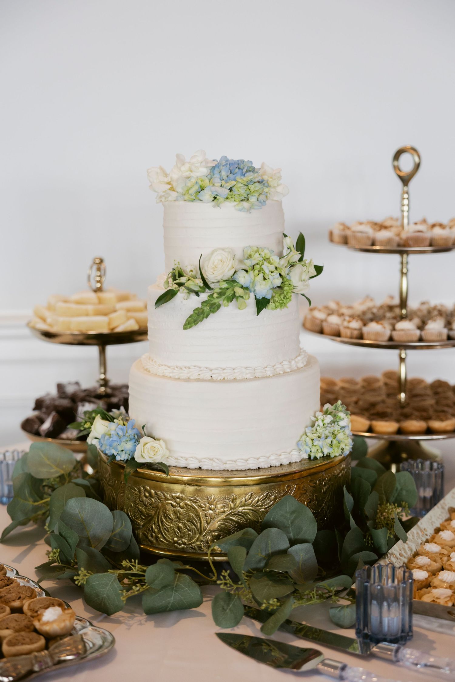 Elegant wedding dessert table with white cakes, greenery, and gold cake stands.