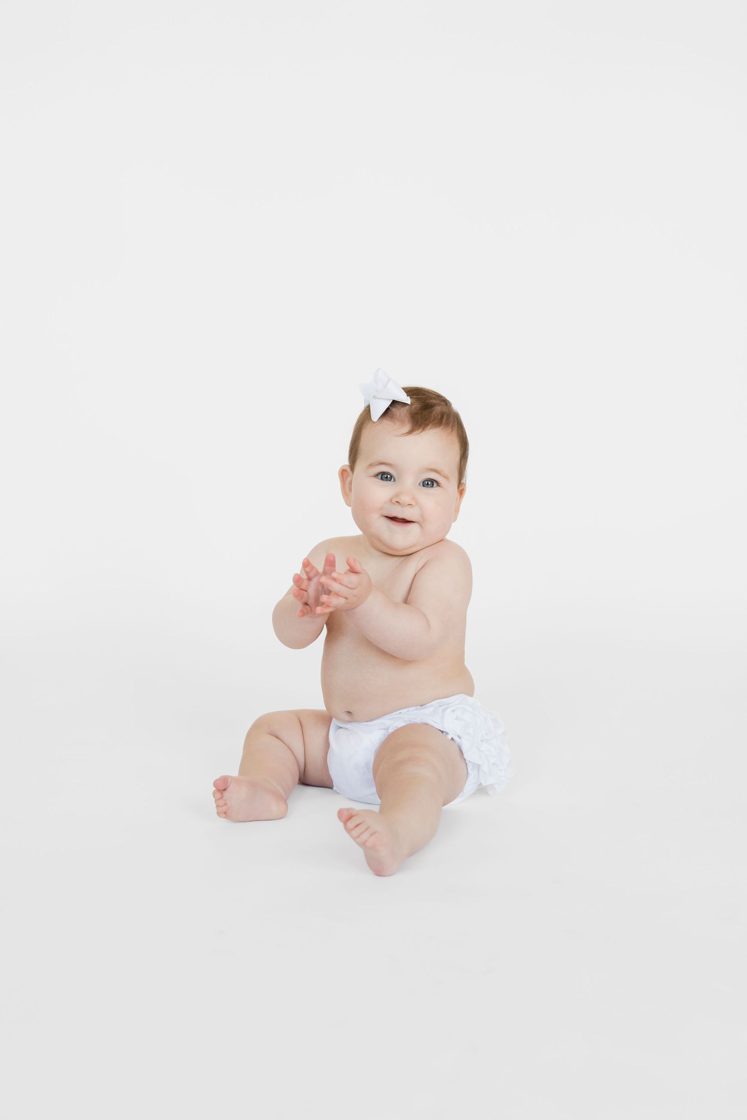 Baby in white diaper sitting and playing against white background.