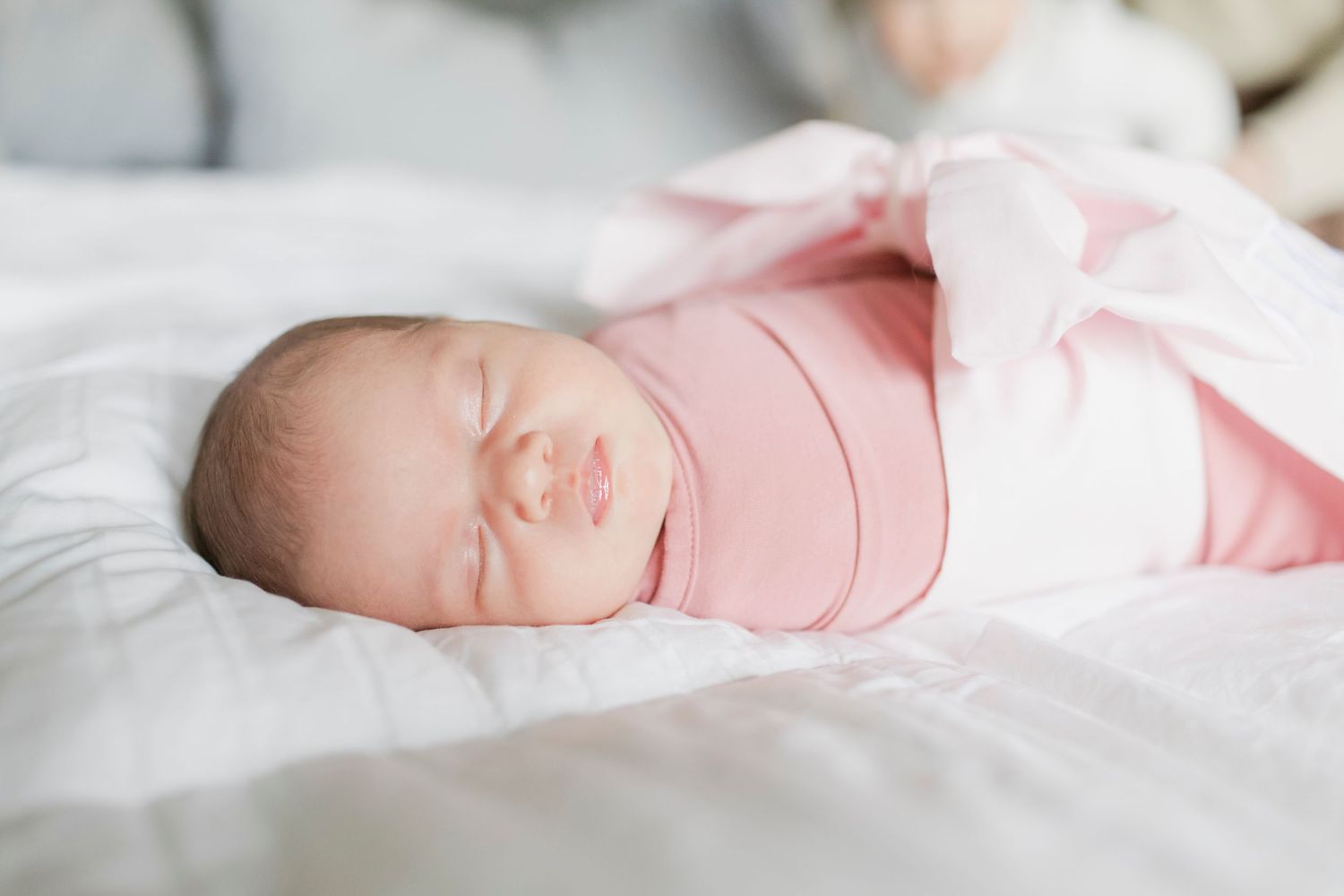 A peaceful newborn baby sleeps soundly wrapped in pink and white clothing.