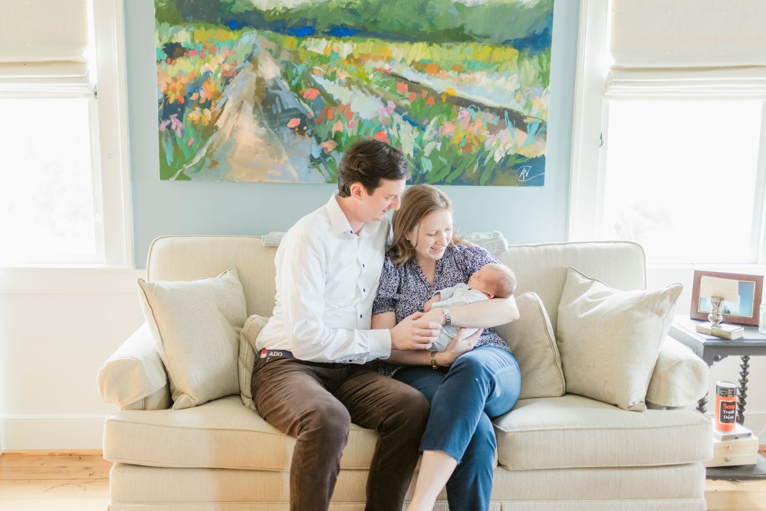 Family relaxing together on a couch in a bright room with landscape artwork.