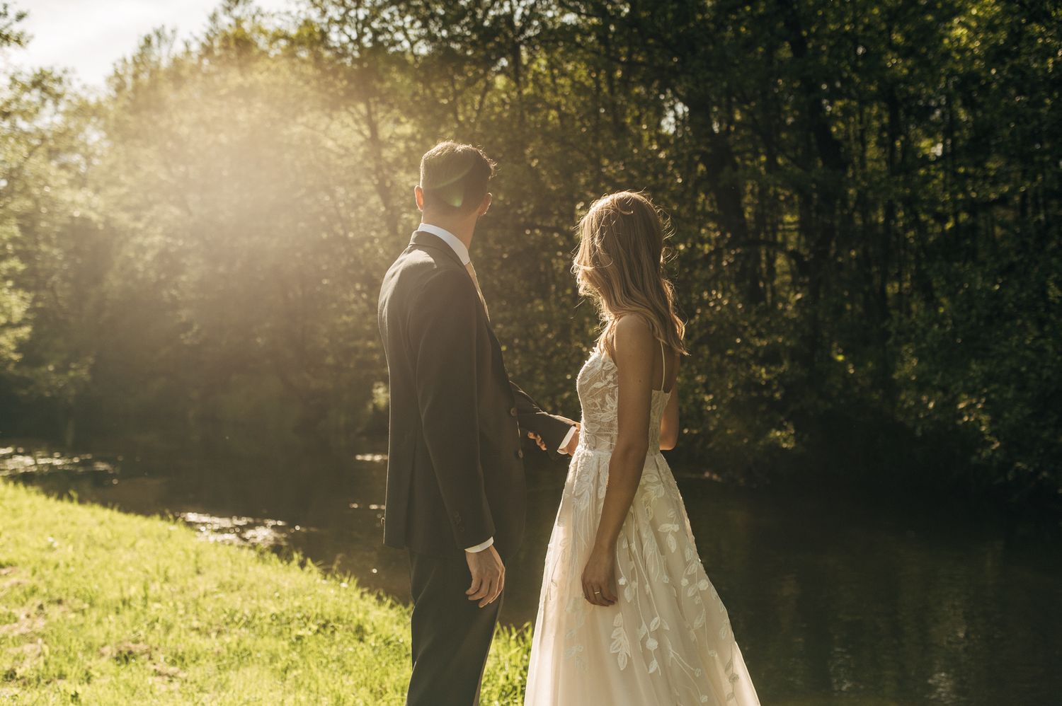 Romantic wedding couple embraces in sunlit garden setting with dreamy bokeh effect in background.