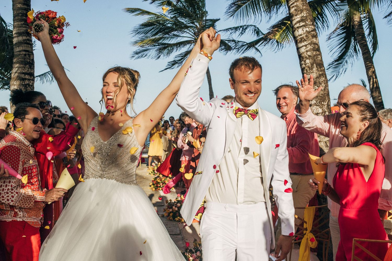 Joyful wedding celebration with palm trees swaying in the background on a tropical beach.