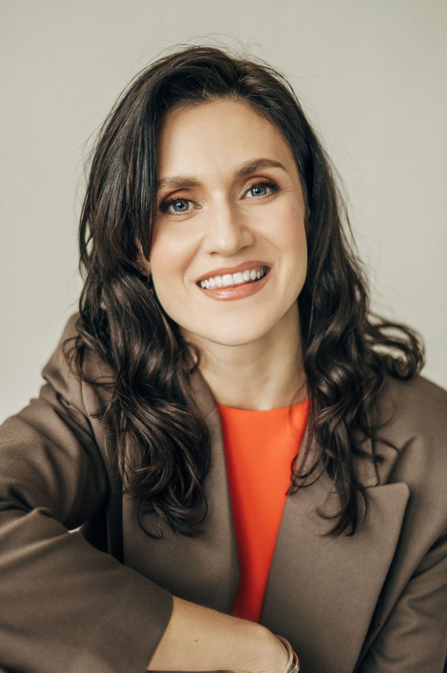 Studio portraits in brown jacket and orange top with expressive smiles.