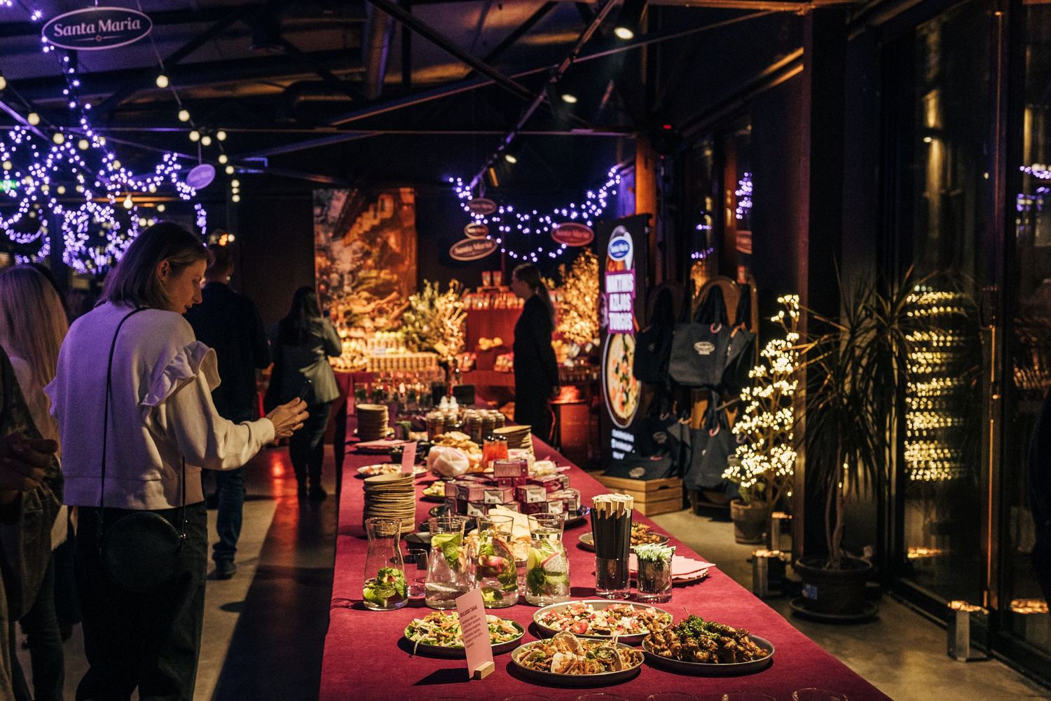 Holiday decorations and twinkling lights illuminate a dark indoor market space with festive displays and vendors.