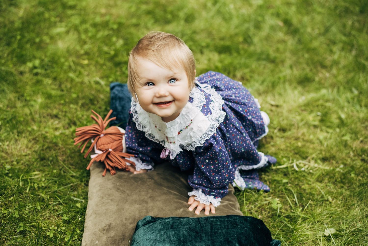 A happy toddler in a navy blue dress crawls on the grass outdoors.