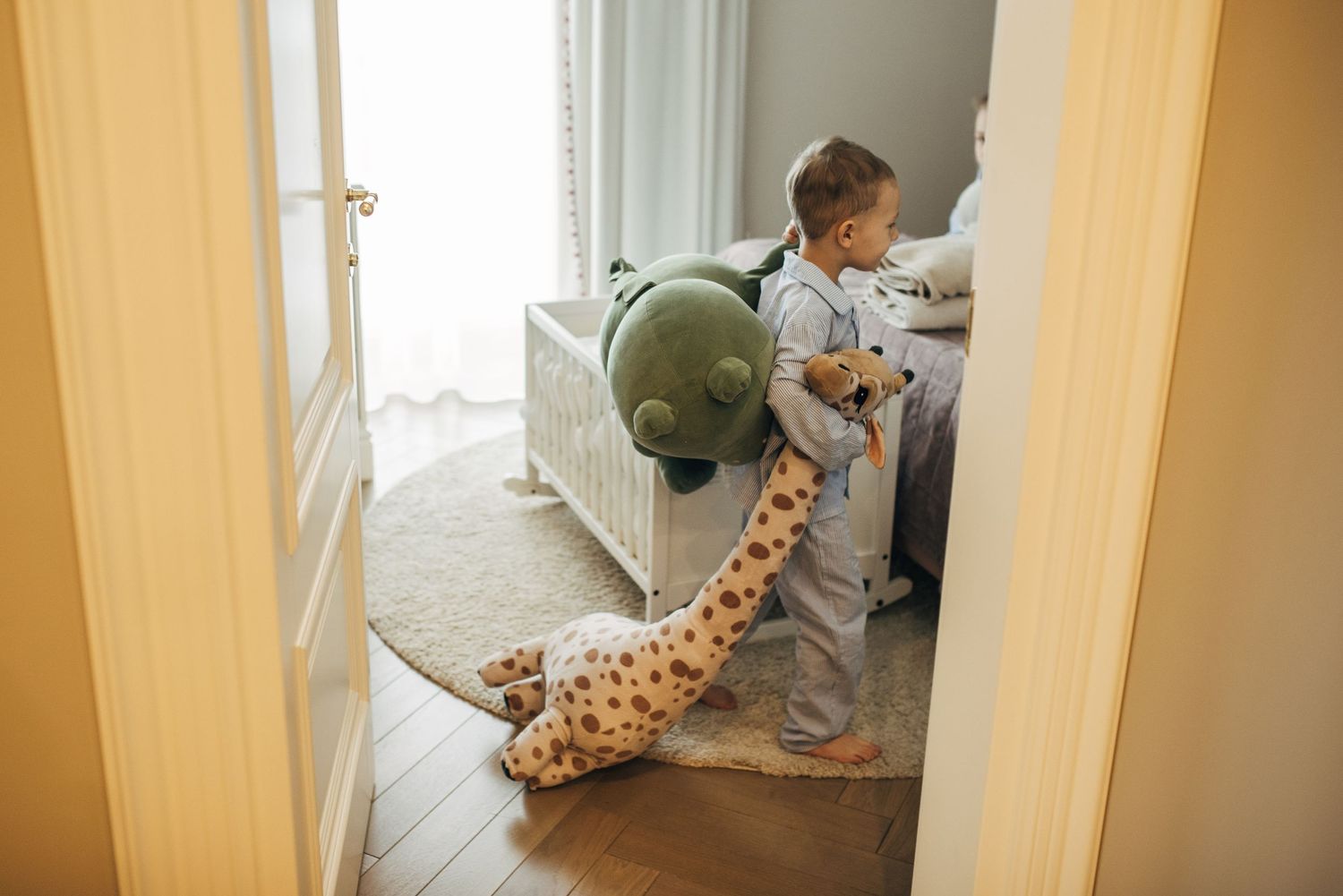 Child playing near doorway with stuffed giraffe toy visible in background.