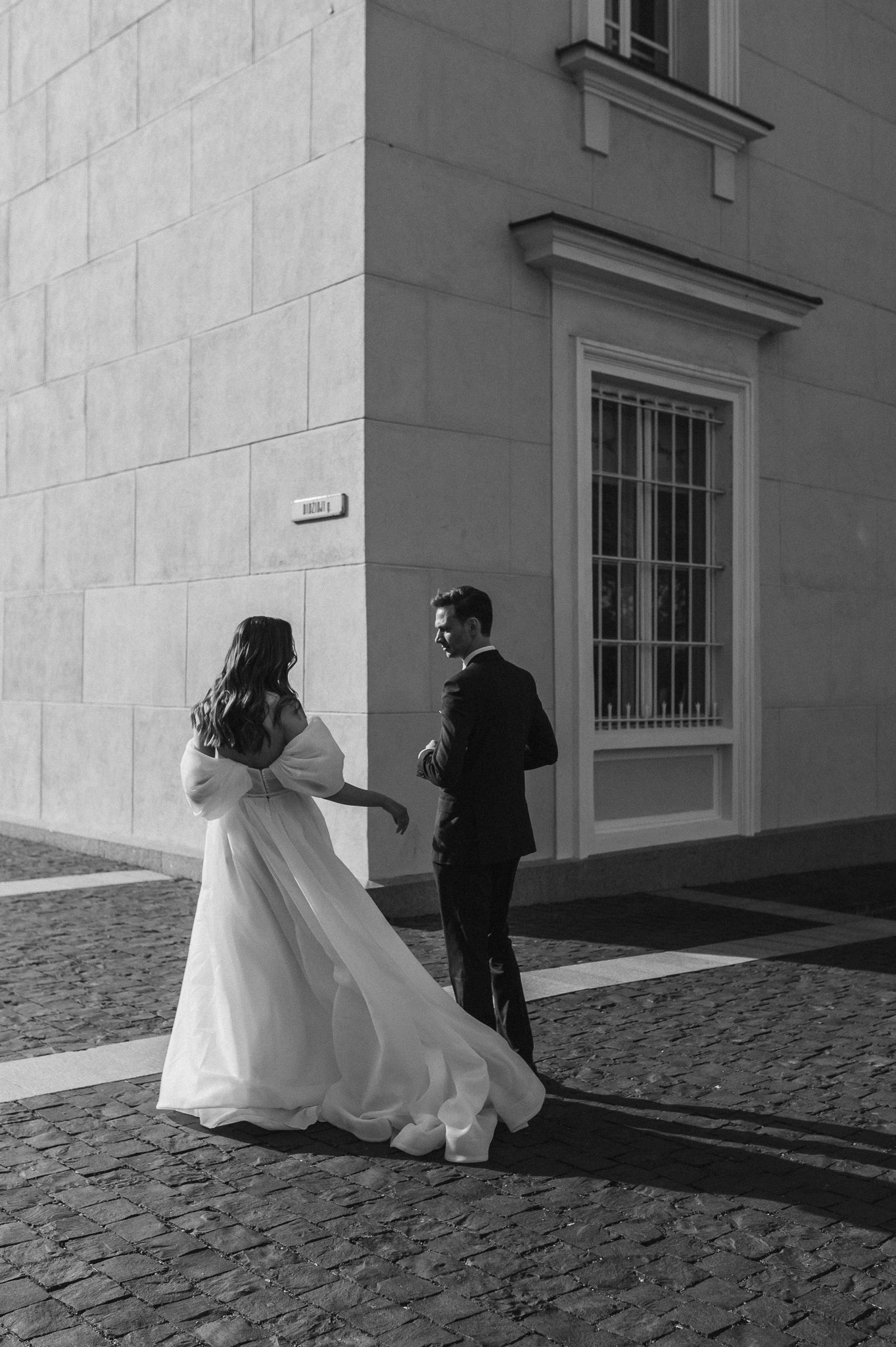 Black and white photo series of newlyweds running playfully on cobblestone street.