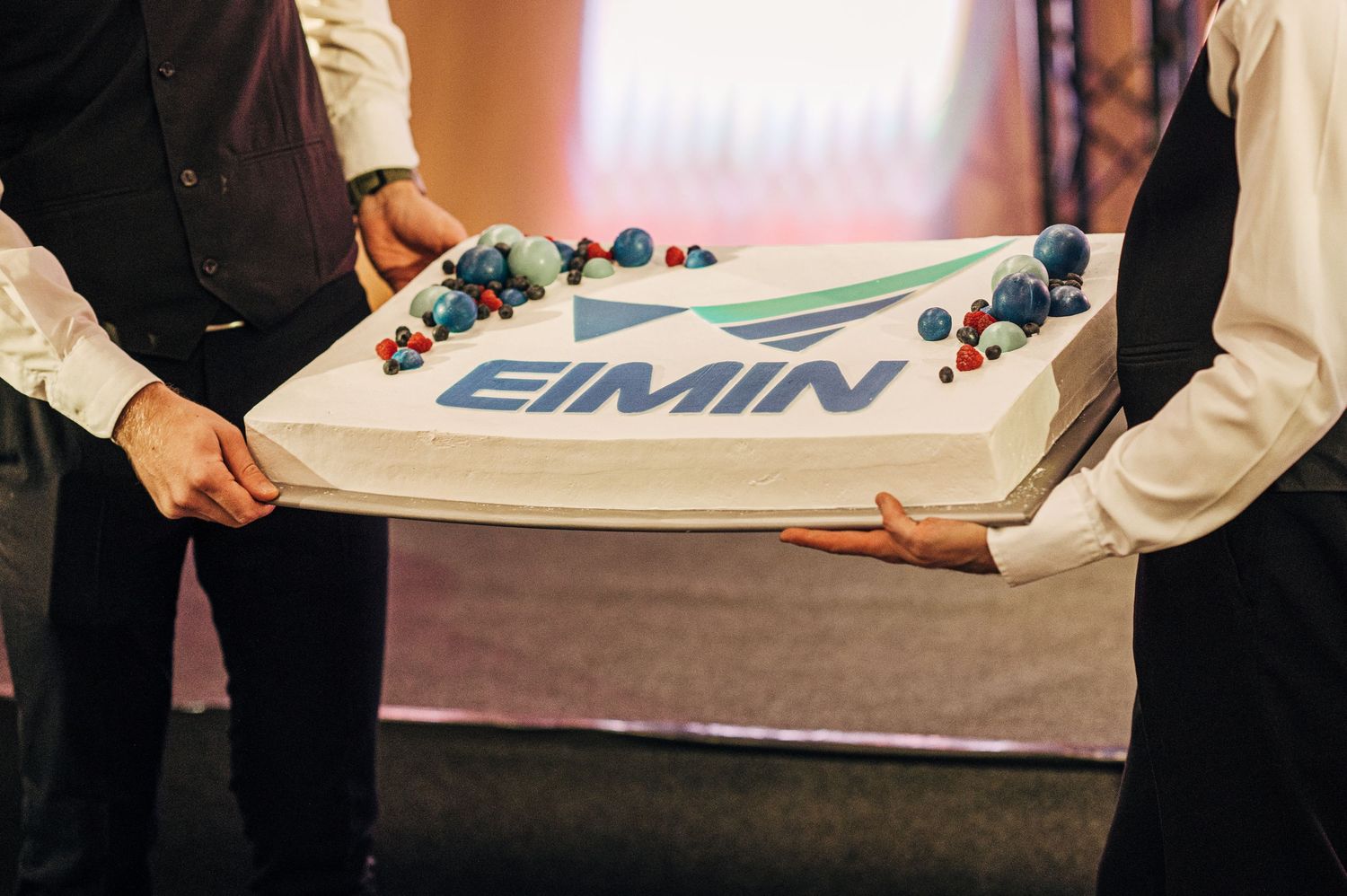 Event staff members holding a branded banner at an indoor corporate gathering.