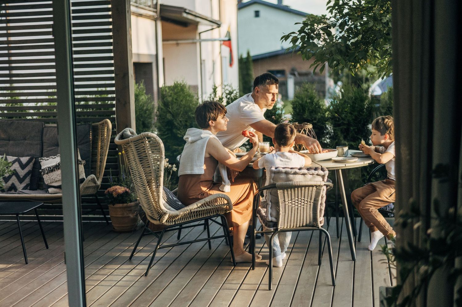 People gather on an outdoor patio with chairs and tables under natural shade.