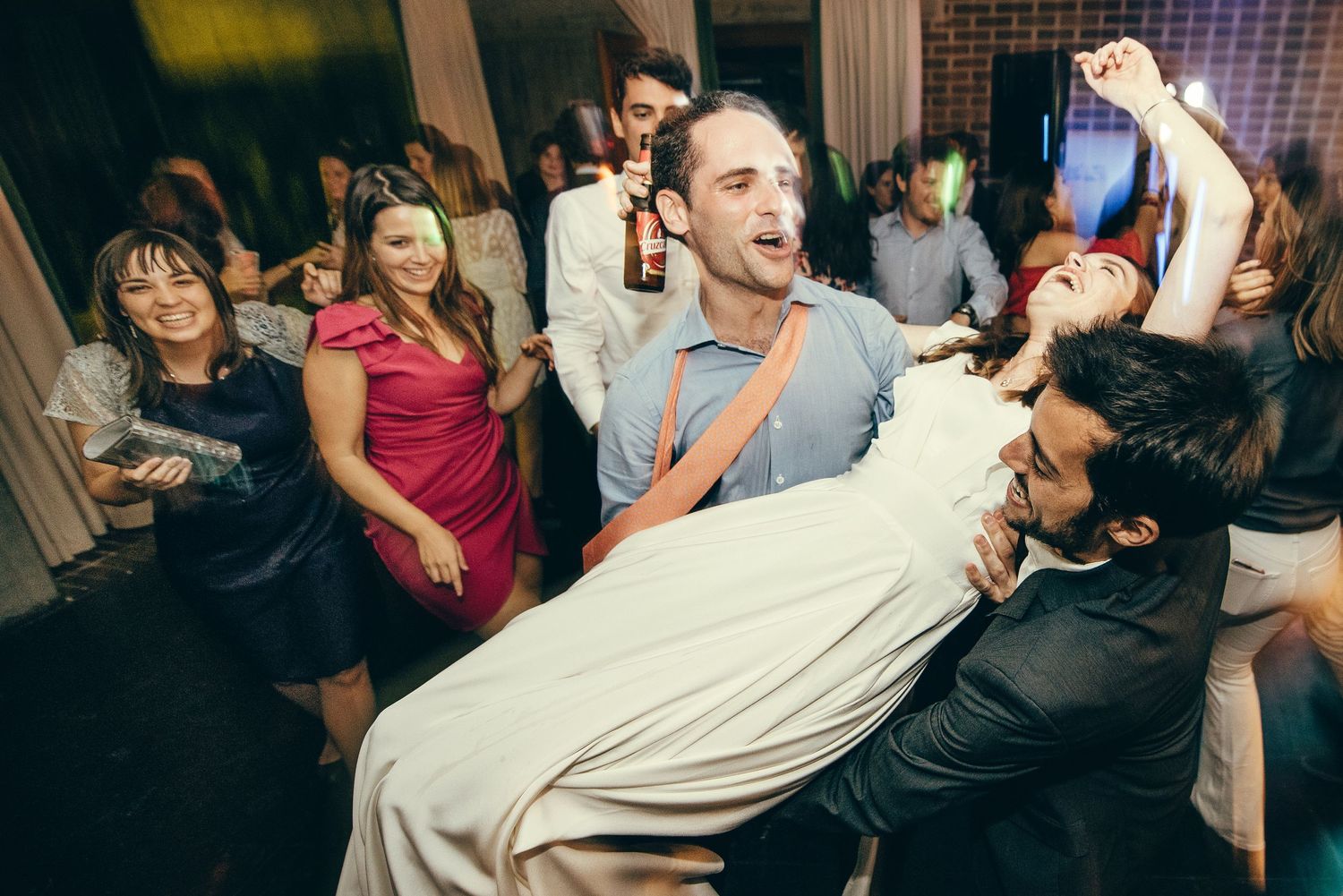 Wedding celebration with guests dancing energetically at an indoor reception venue.