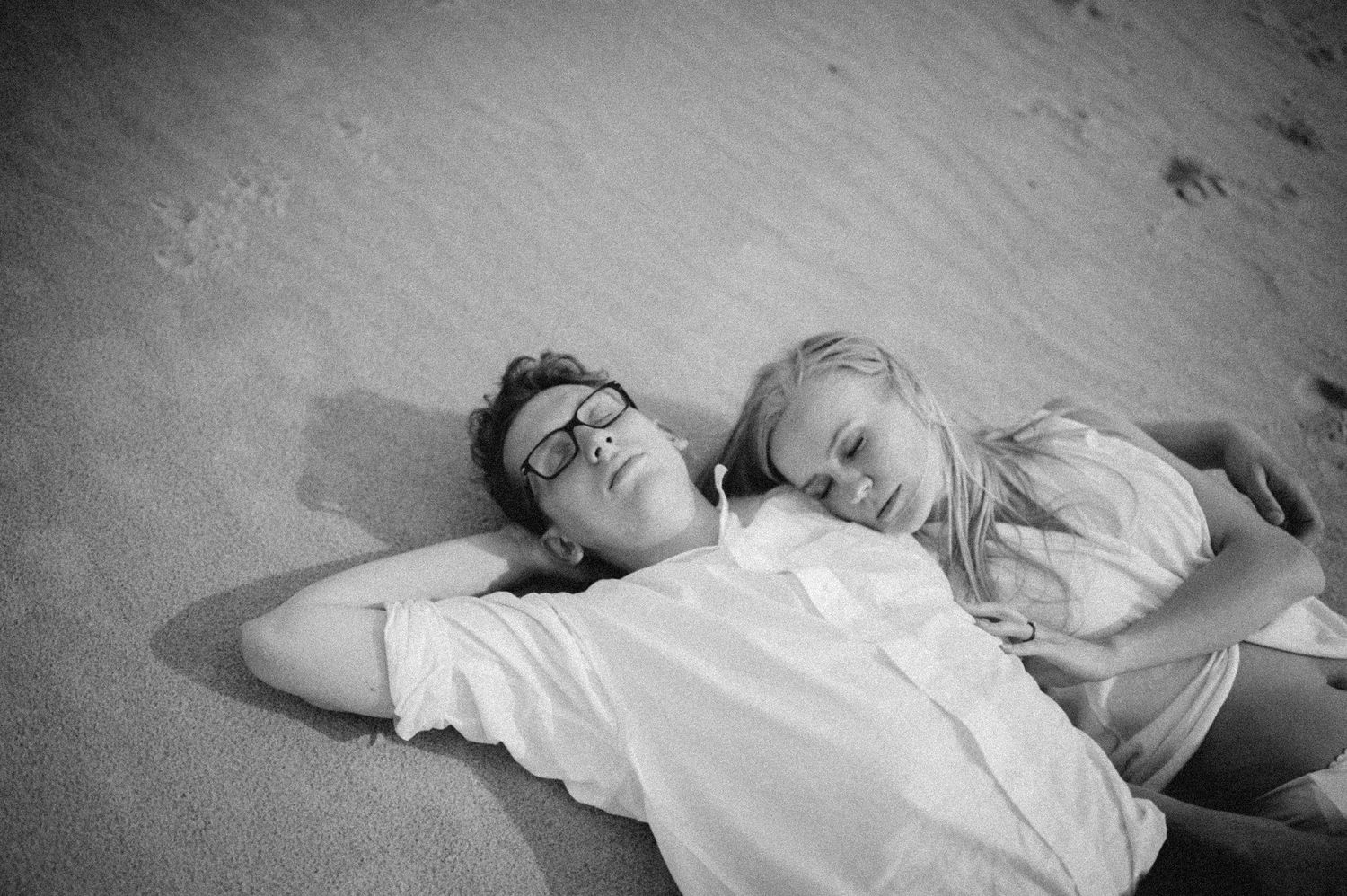 A black and white photo of a couple lying together on sand.
