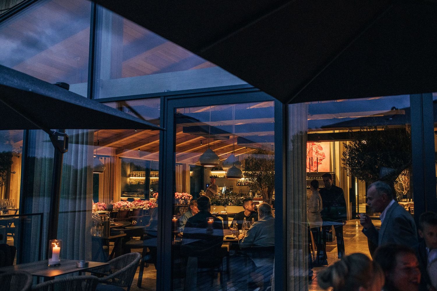 Restaurant diners enjoy panoramic sunset views through floor-to-ceiling windows in an elegant waterfront setting.