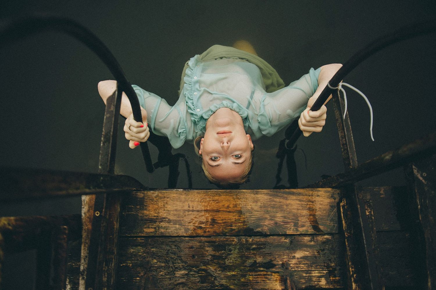 Person hanging upside down from wooden beam in dark atmospheric setting.