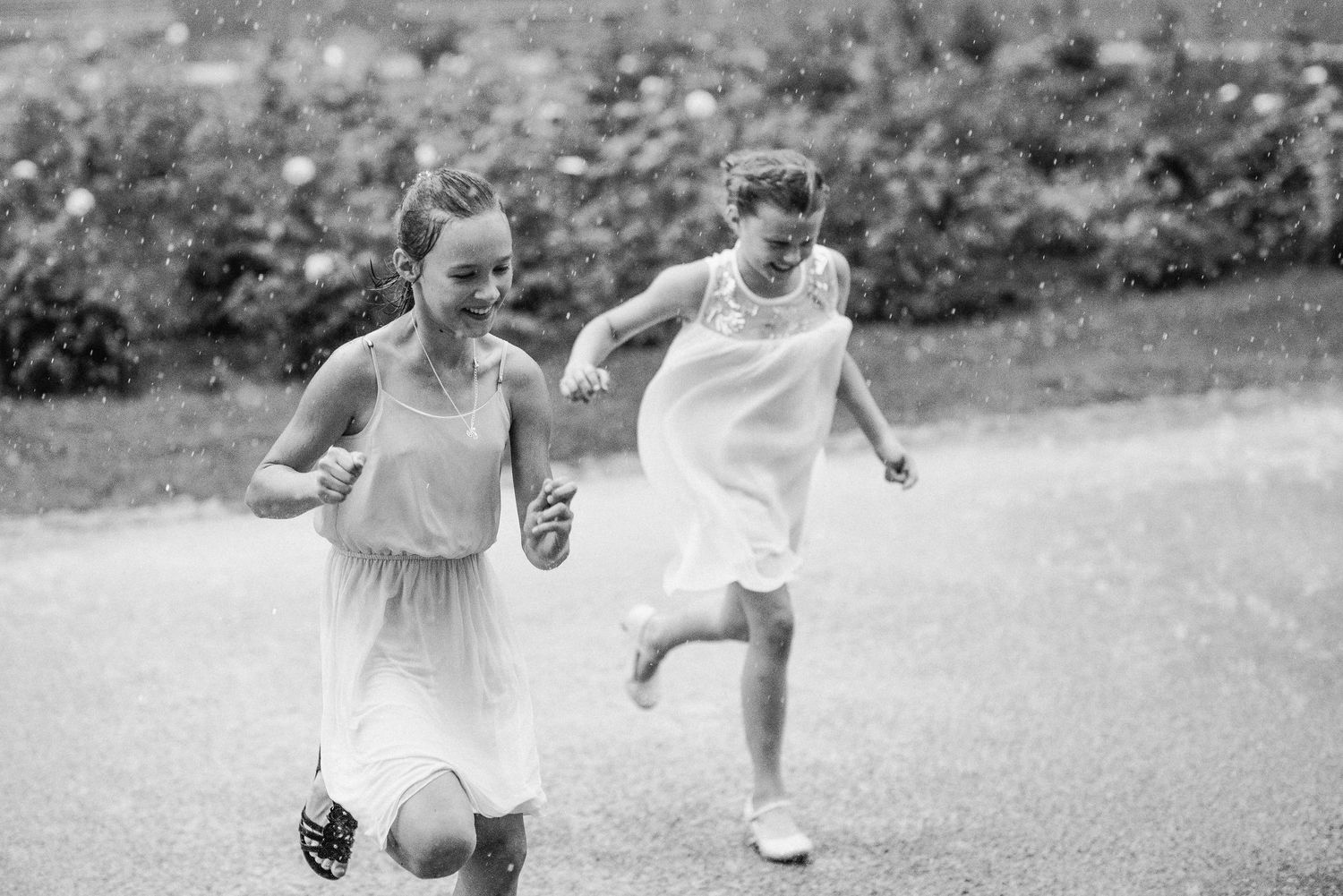 Two children laugh and run together on a path in black and white photography.