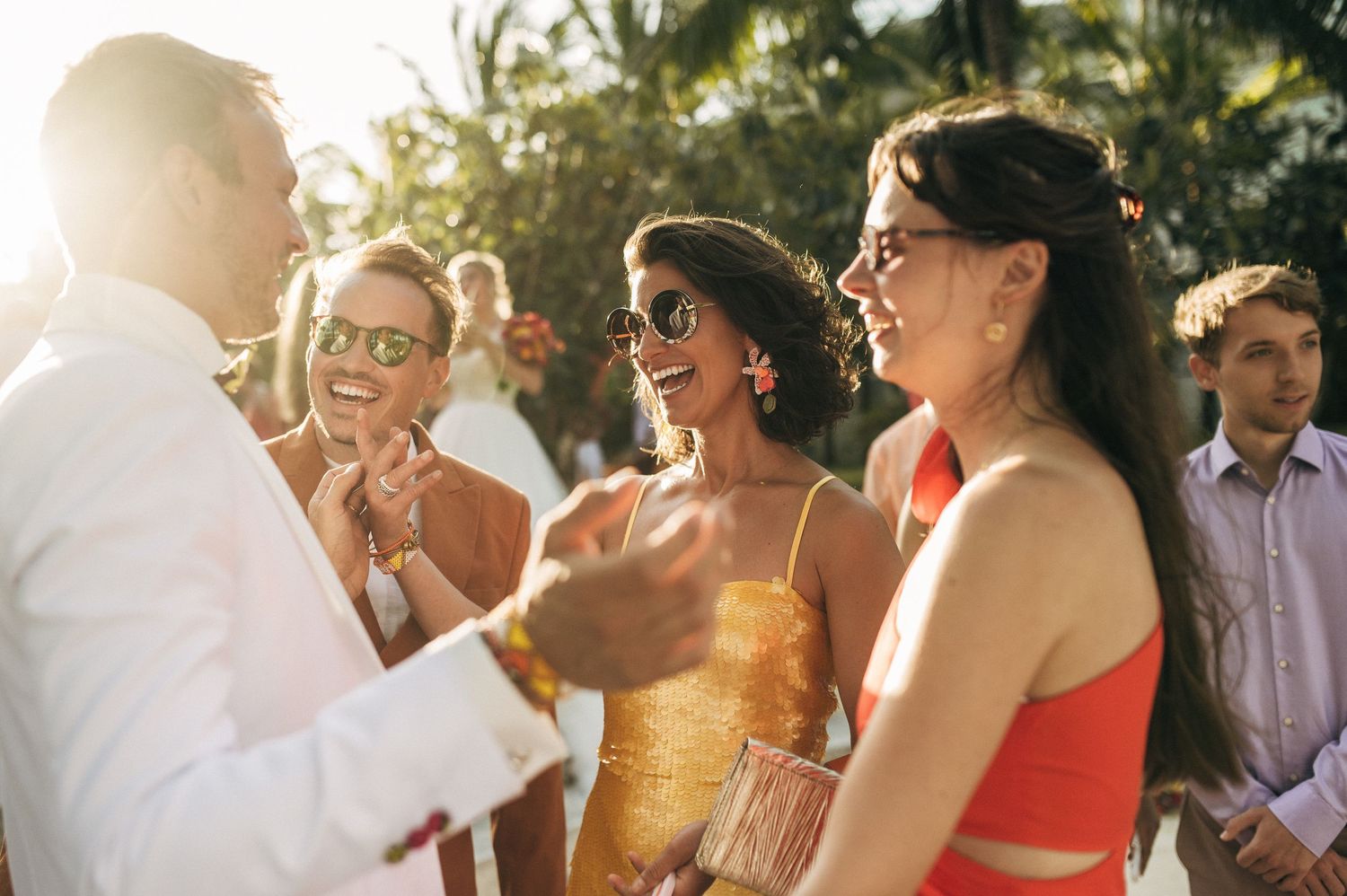 Wedding guests laugh and smile together during an outdoor celebration in golden sunlight.