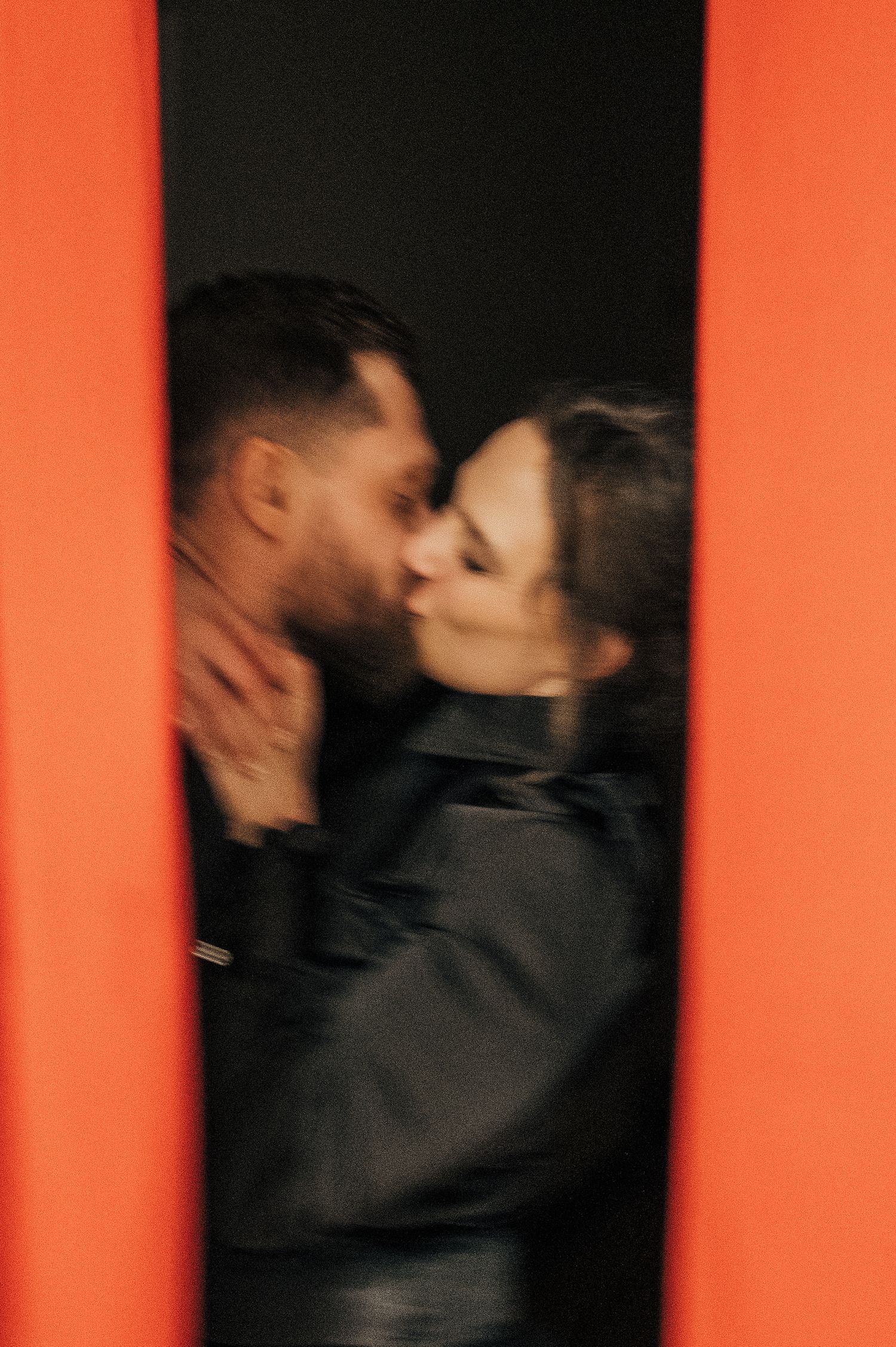 Abstract motion blur photography against bold orange backdrop showing silhouettes in embrace.