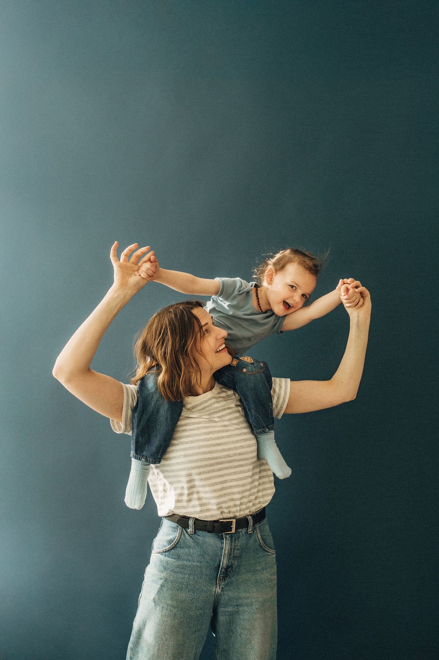 Playful dance poses against dark teal wall showing joyful movement.