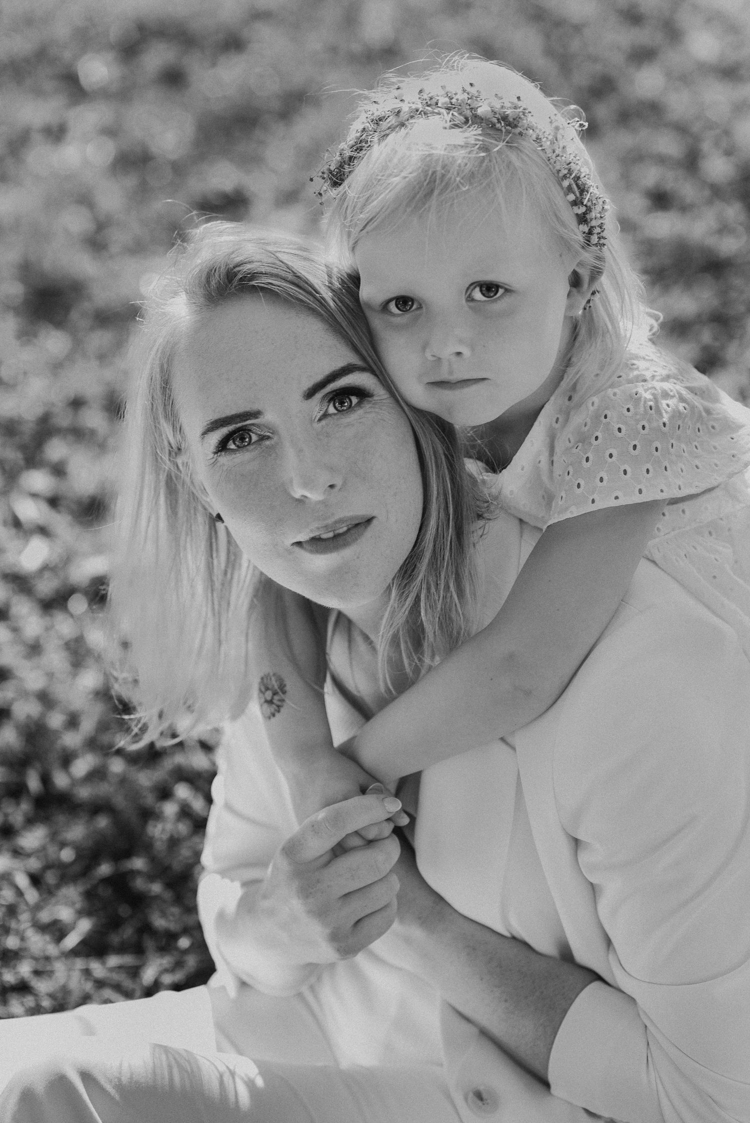 Black and white portrait of a blonde mother and young daughter embracing outdoors.