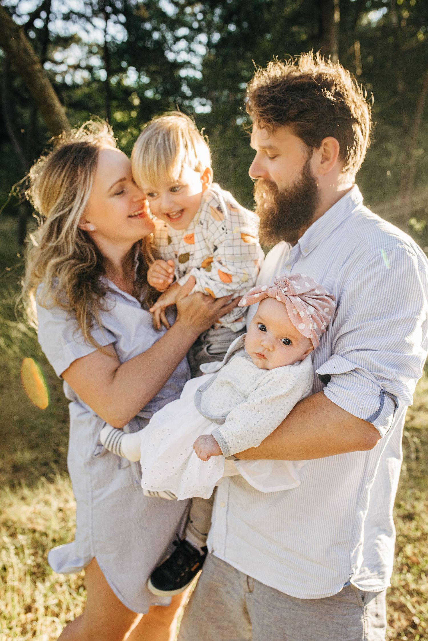Family wearing white and light colors sharing playful moments in sunlit outdoor setting.