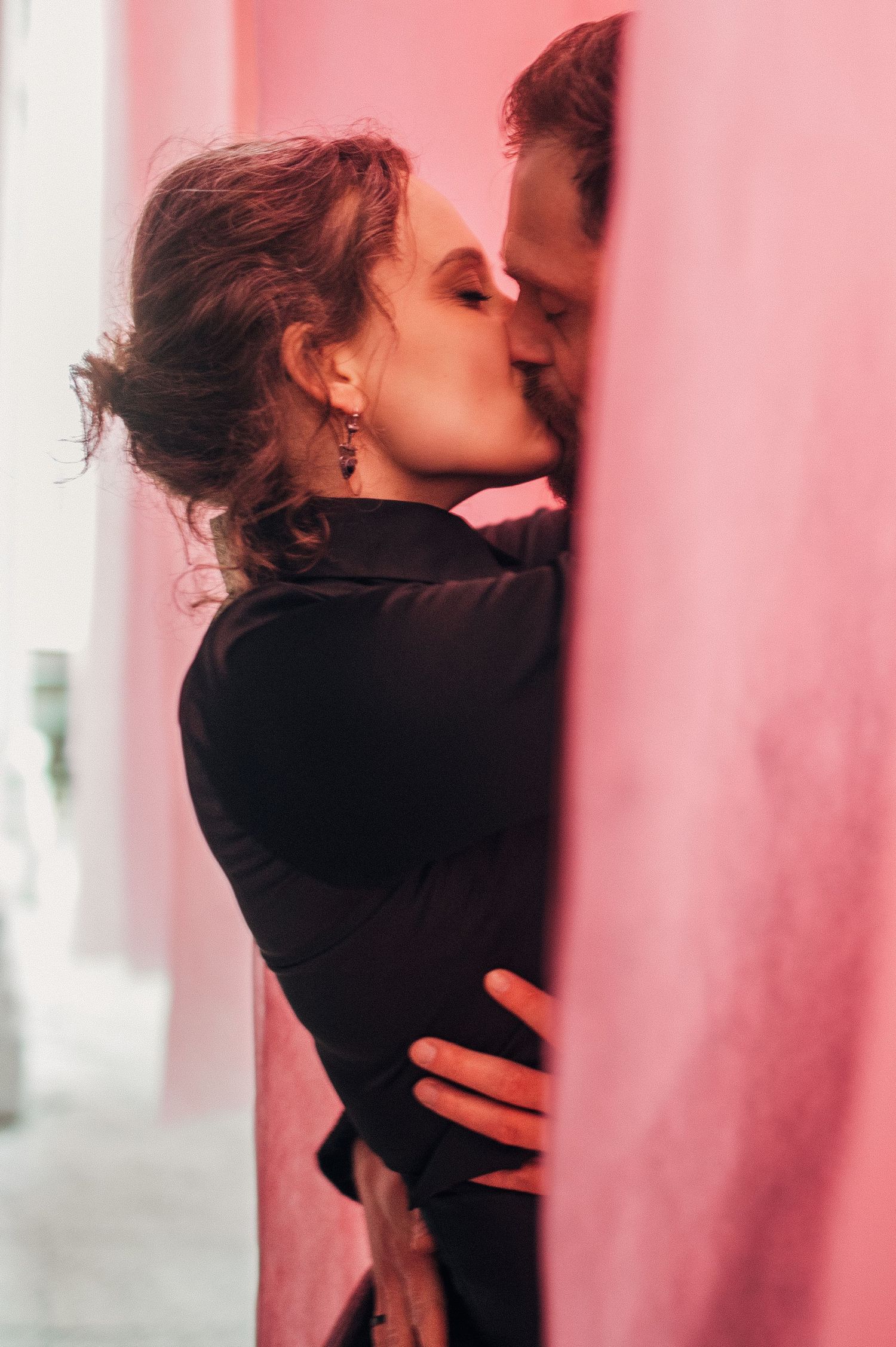 Intimate romantic moment framed by pink curtains and columns.