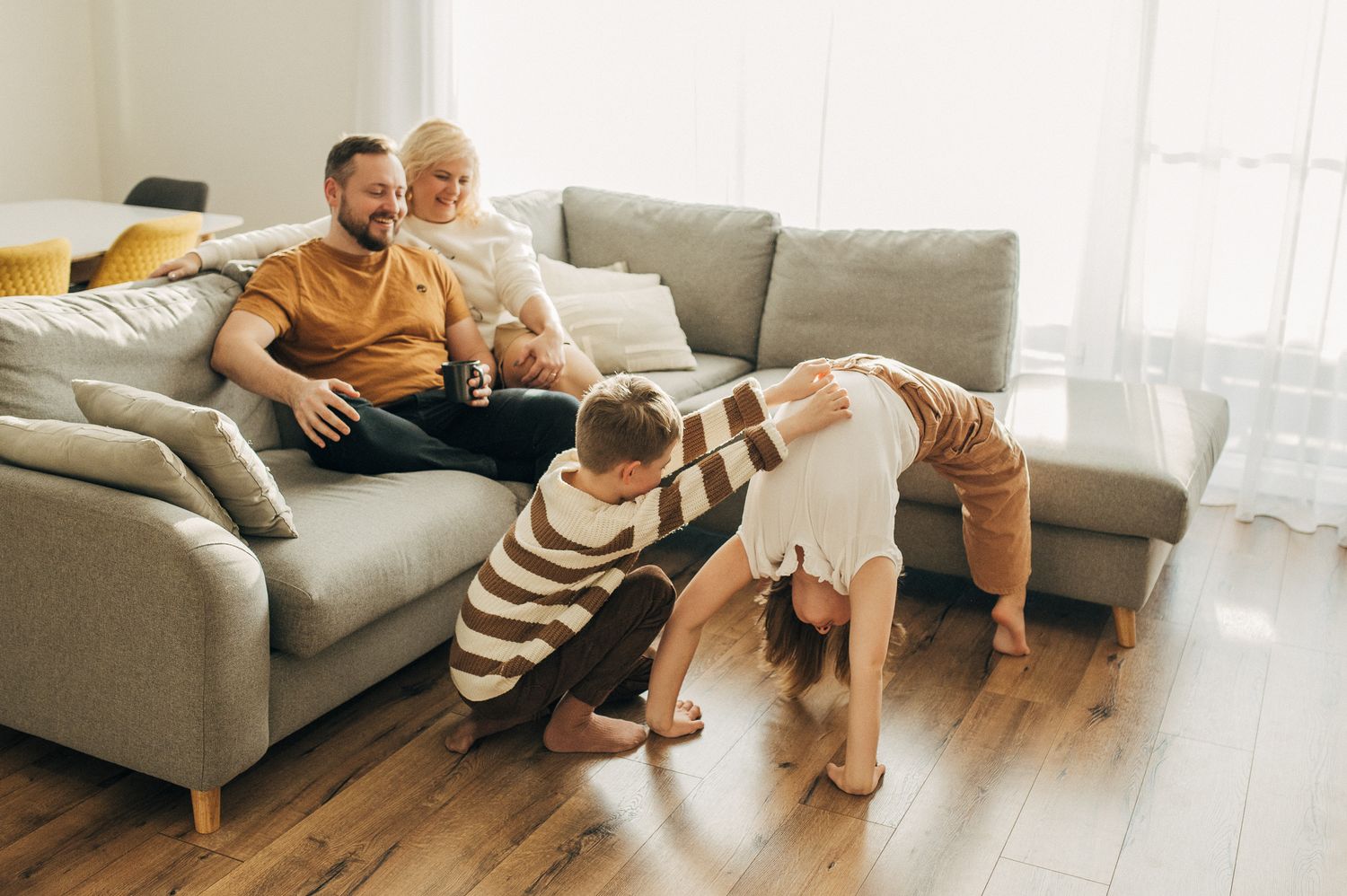 Candid moments of family bonding and playing on floor near grey couch in bright room.