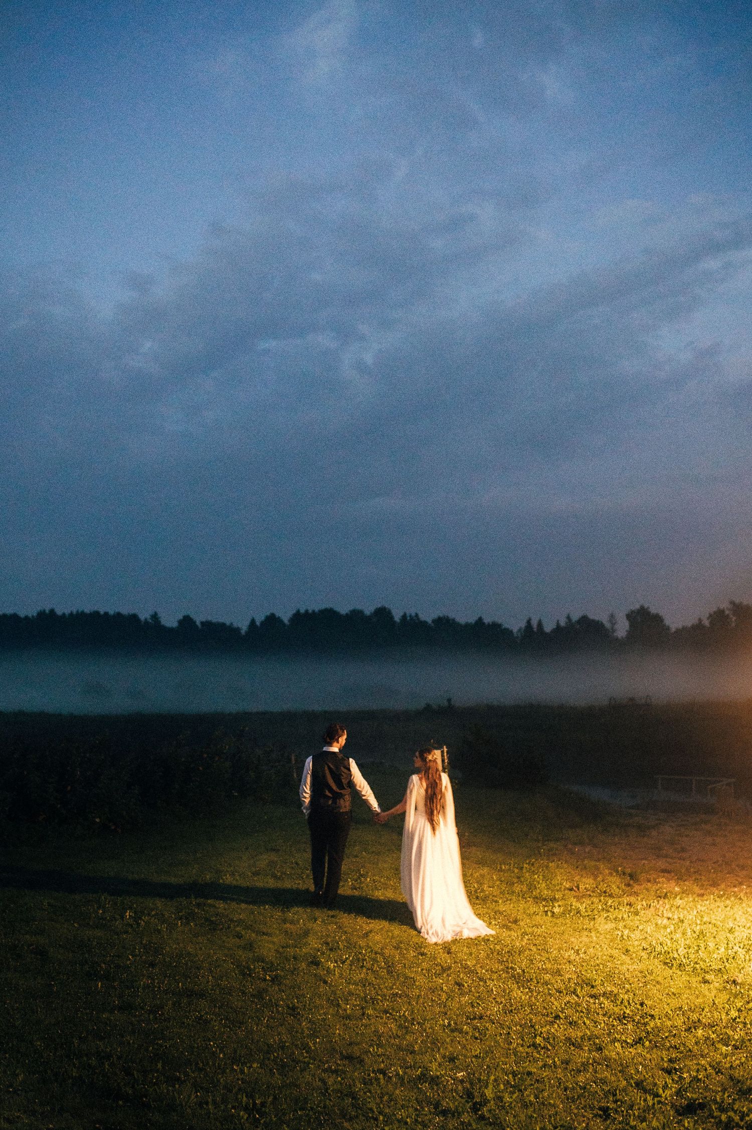 Wedding photos captured at night with dramatic lighting illuminating a couple on a dark field.