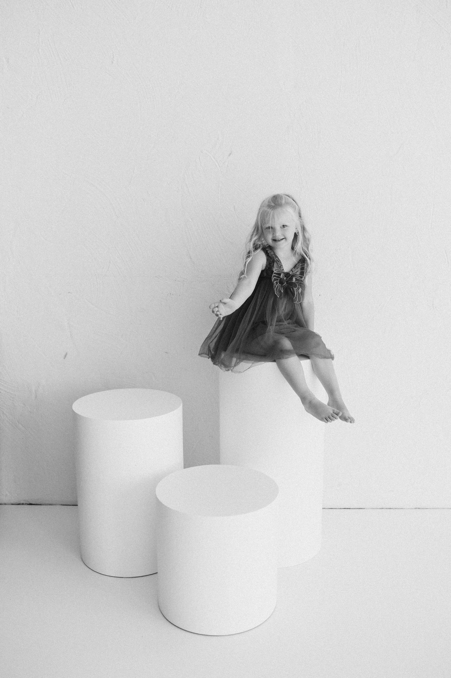 A minimalist black and white photo series showing a figure interacting with white cylindrical pedestals.
