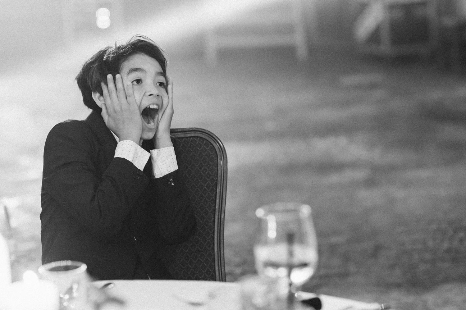 Black and white photo of surprised man with hands on face sitting at a dinner table.
