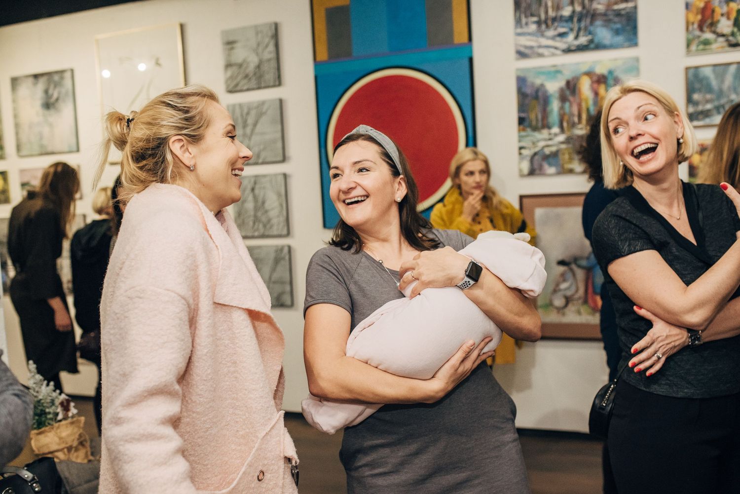 People laughing and embracing at a casual gathering with artwork displayed on walls.