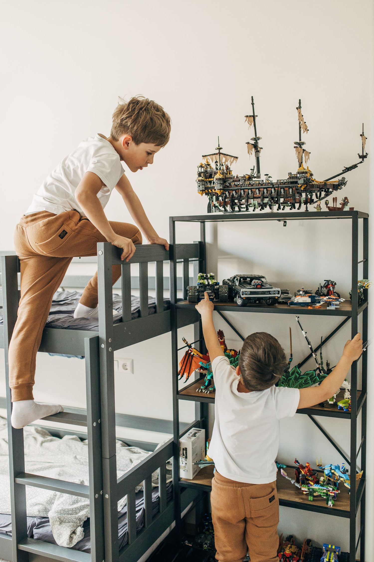 Children playing with model ships and toys displayed on gray shelving units.
