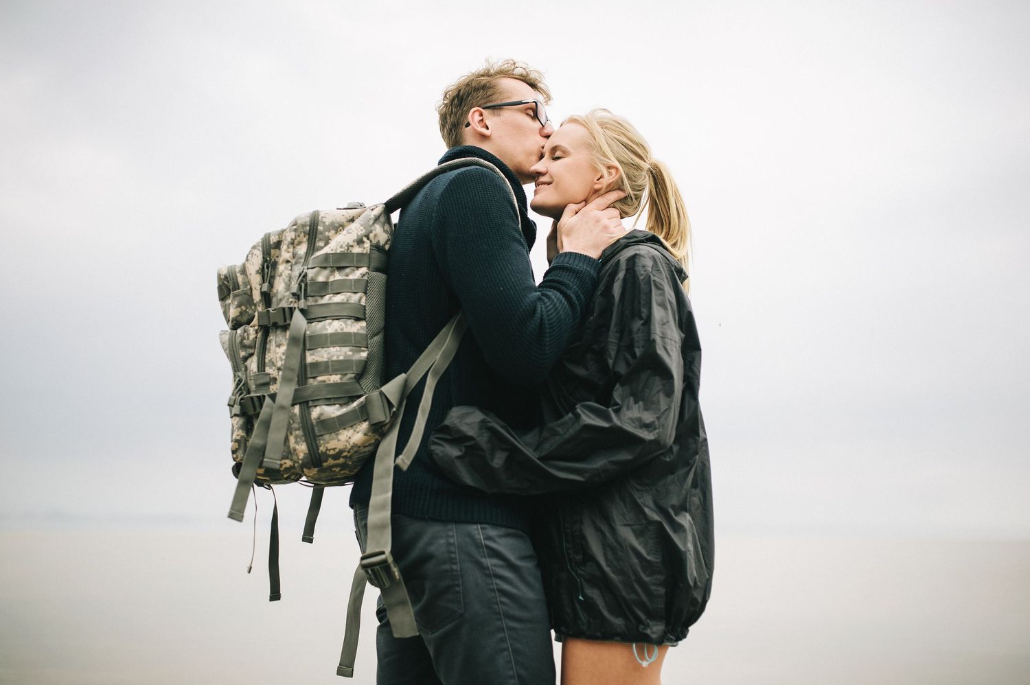 Couple embracing against cloudy sky with backpacks.